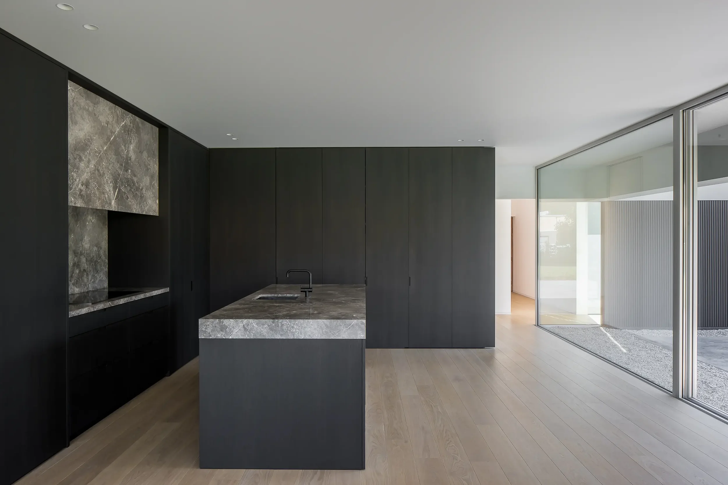 Modern kitchen with dark cabinets, marble countertop, large windows, and wooden flooring.