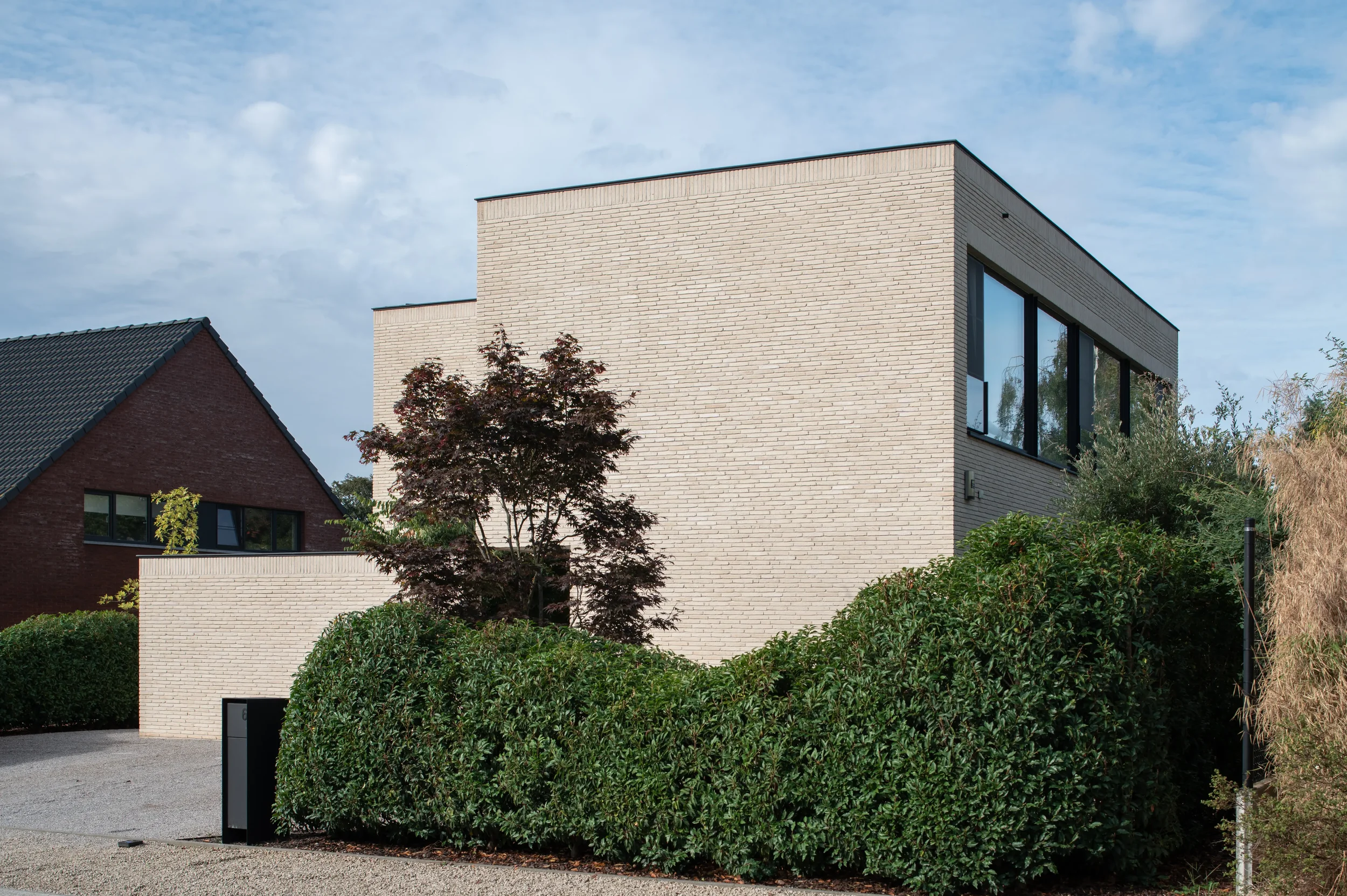 Modern white brick building with large black window frames, surrounded by greenery and trees under a blue sky with scattered clouds.