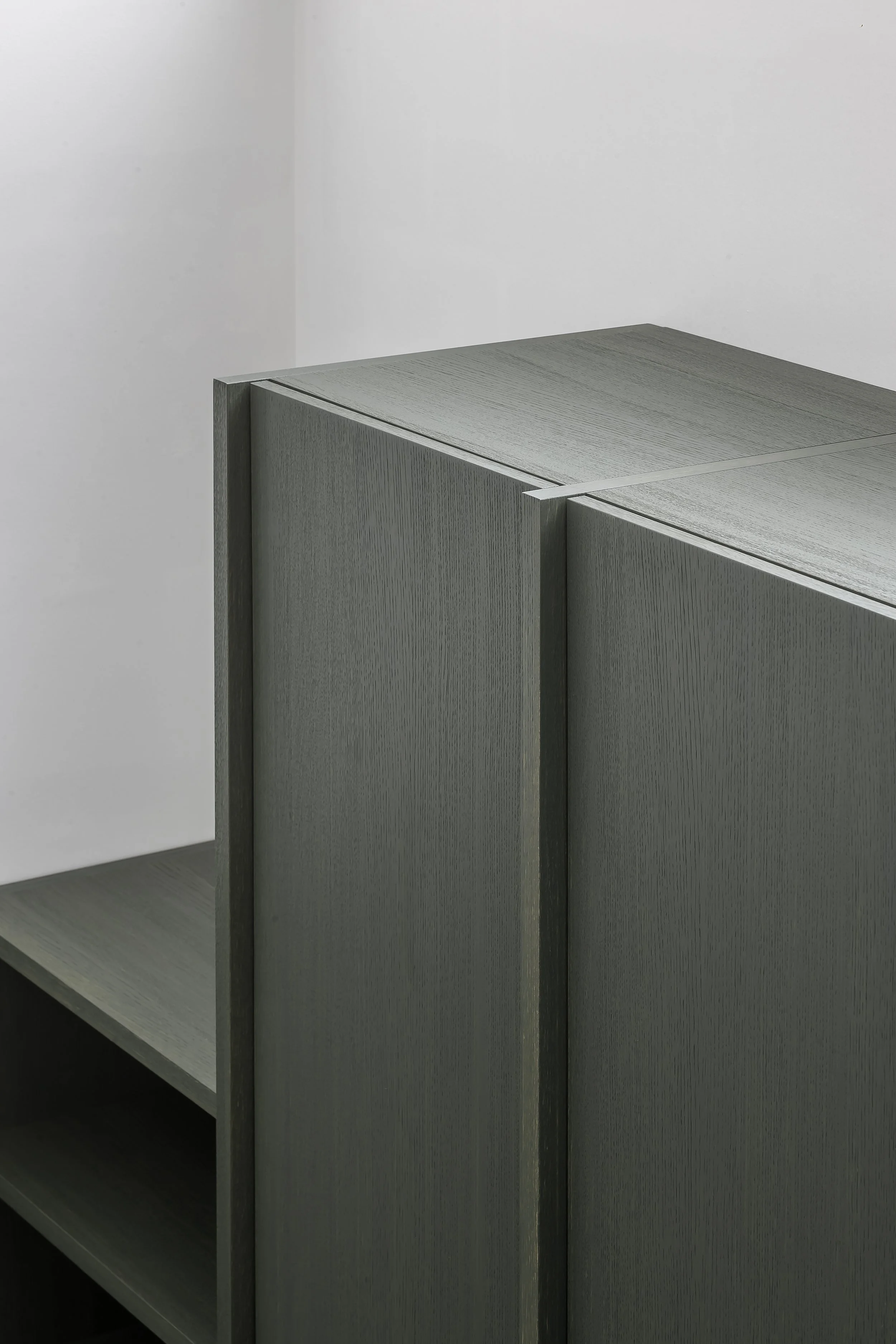 A close-up of a gray wooden bookshelf or cabinet with multiple shelves, positioned against a white wall.