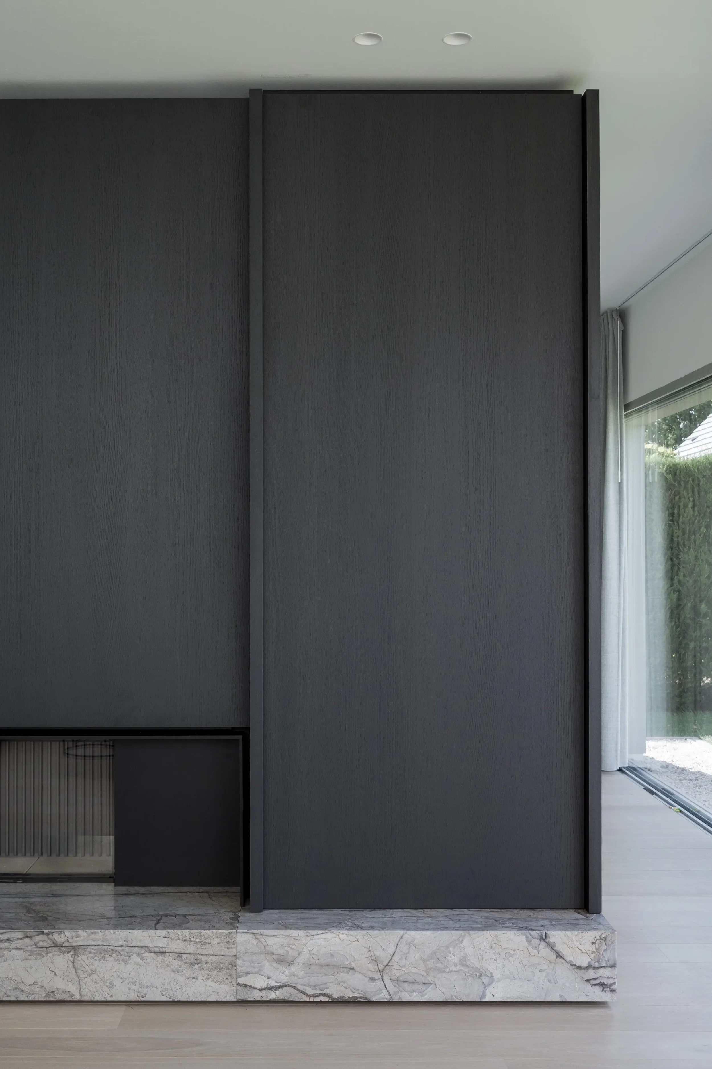 Interior view of a modern room with dark gray partition walls, a marble base, and a window with curtains showing greenery outside.
