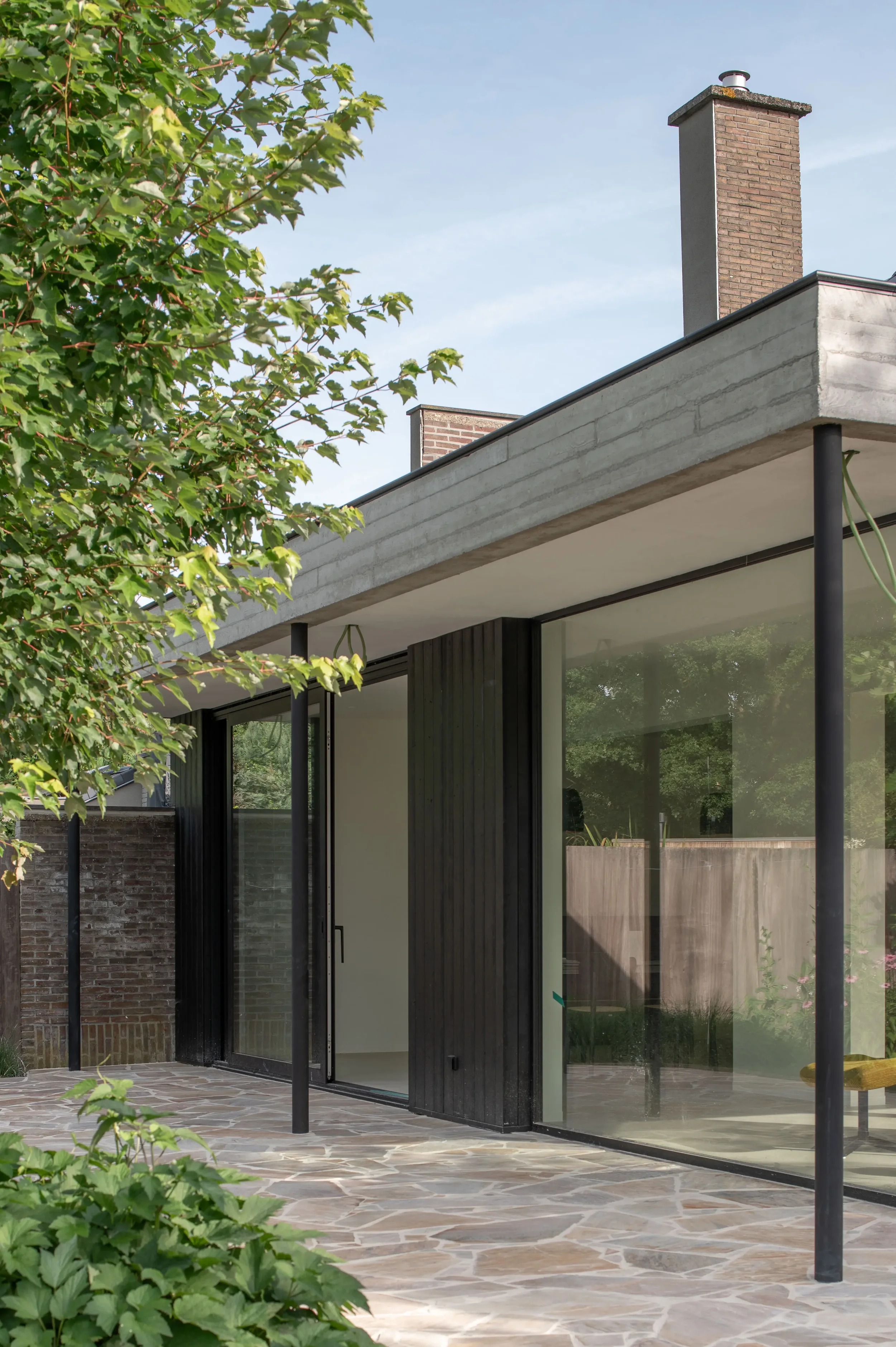 uitbreiding halfopen woning met luifel in zichtbeton en terras in flagstones