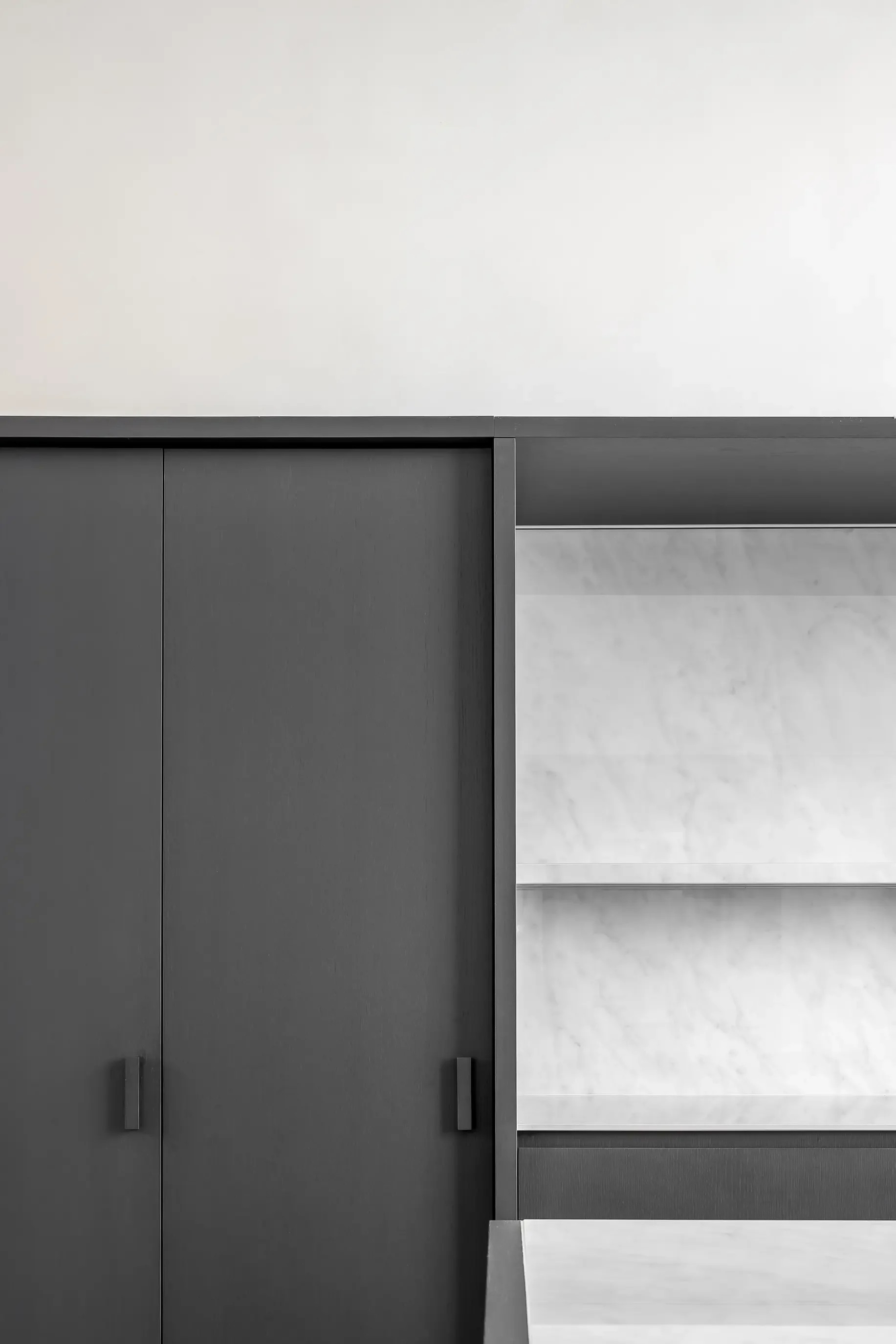 Close-up view of a modern, minimalistic kitchen with dark grey cabinets and white marble walls and floor.