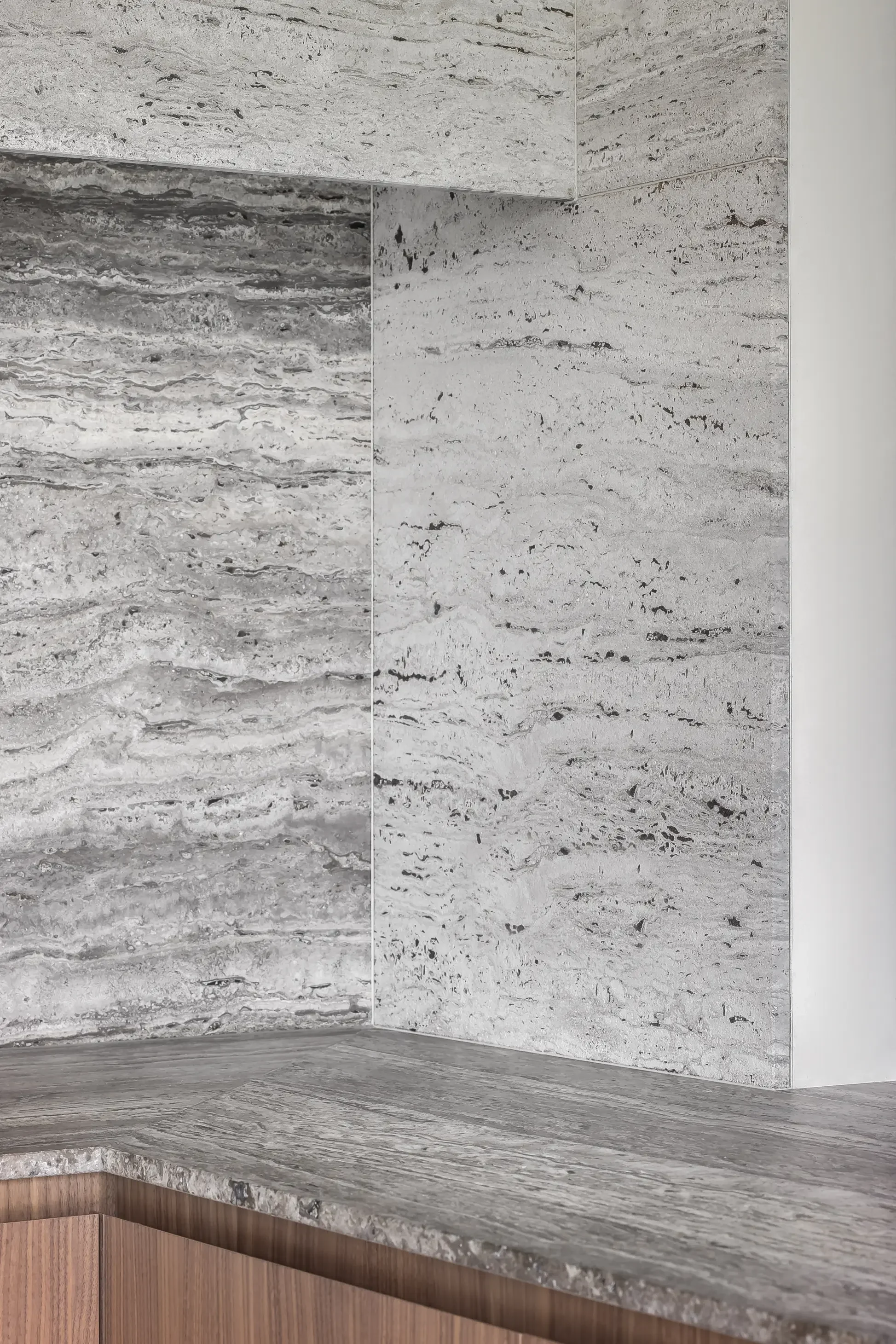 Close-up of a corner of a kitchen countertop made of grey and white marble with a wood cabinet below.