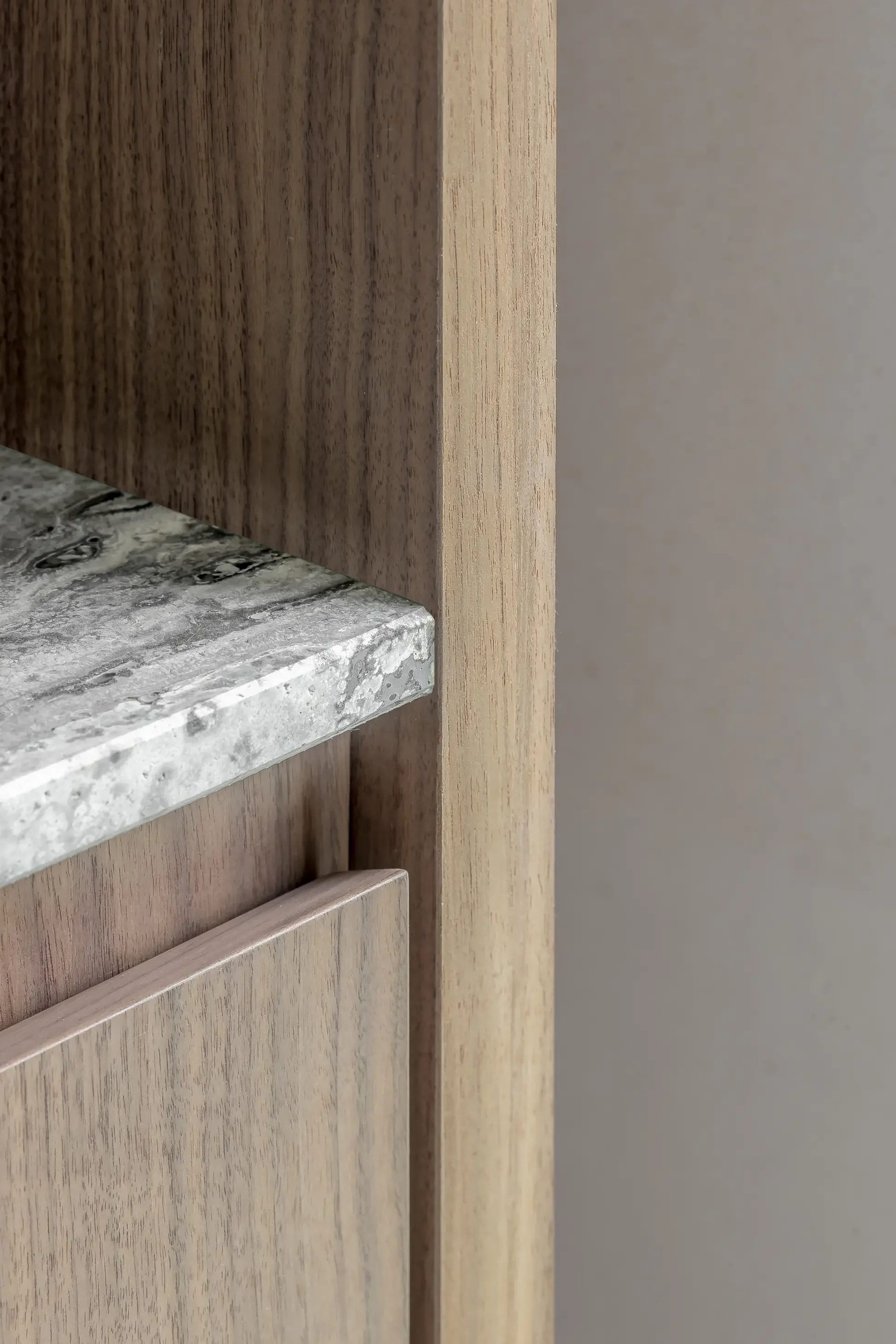 Close-up of a corner of a wooden kitchen cabinet with a gray marble countertop.