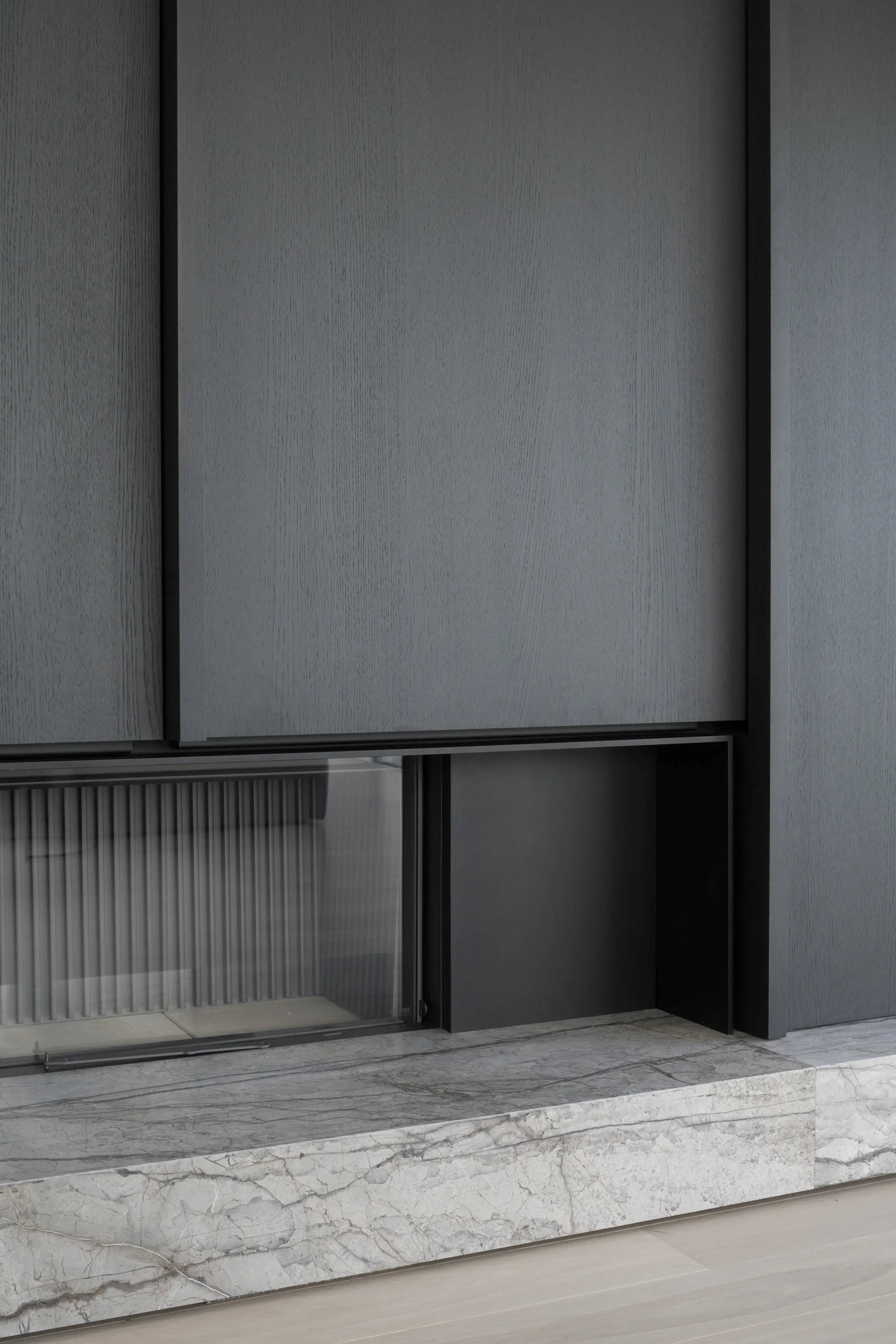 Close-up of a modern, dark gray cabinet with textured surfaces and black framing, positioned on a marble floor with white and gray veining.