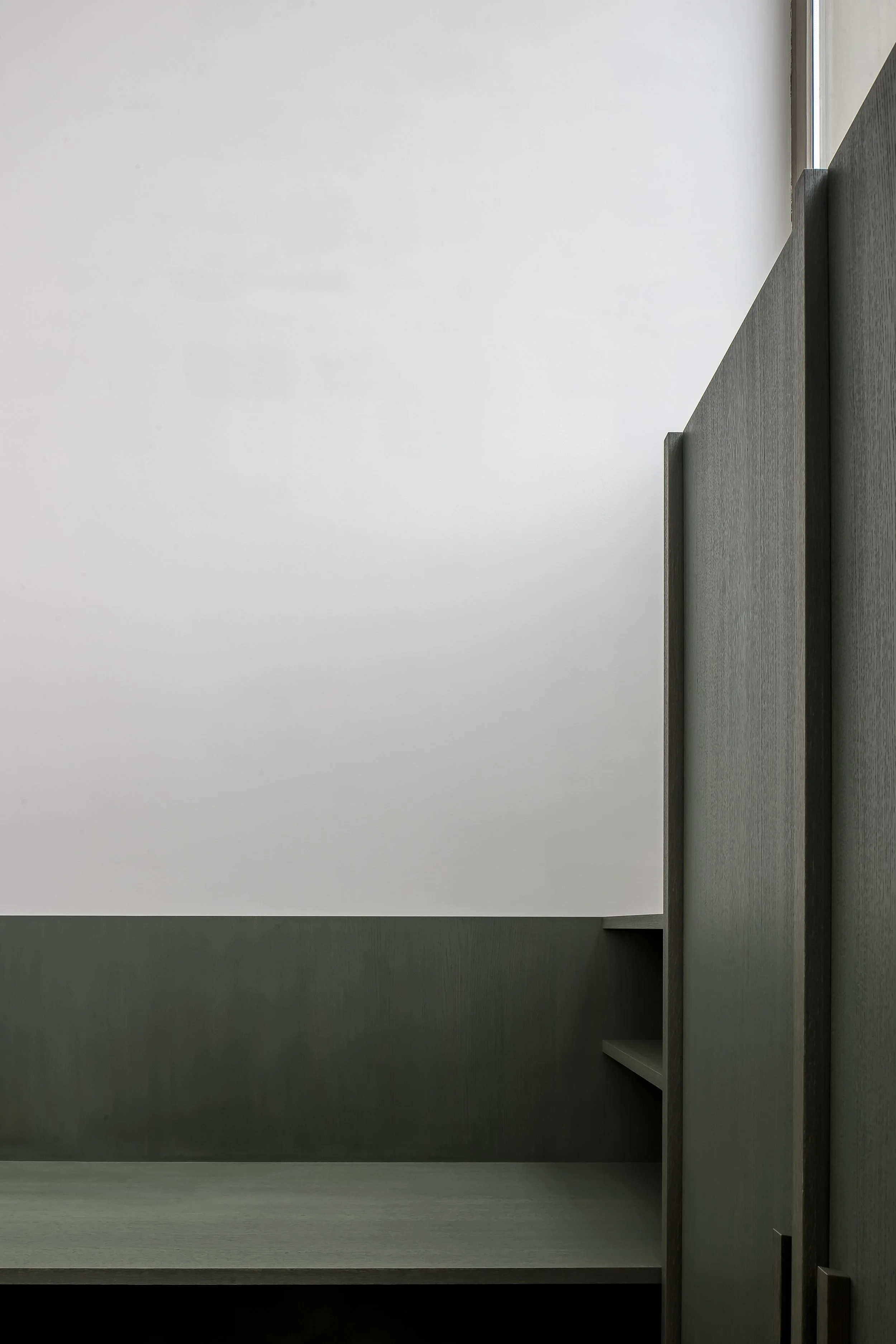 Empty modern room with a white wall, gray cabinets with open shelves, and a small window.