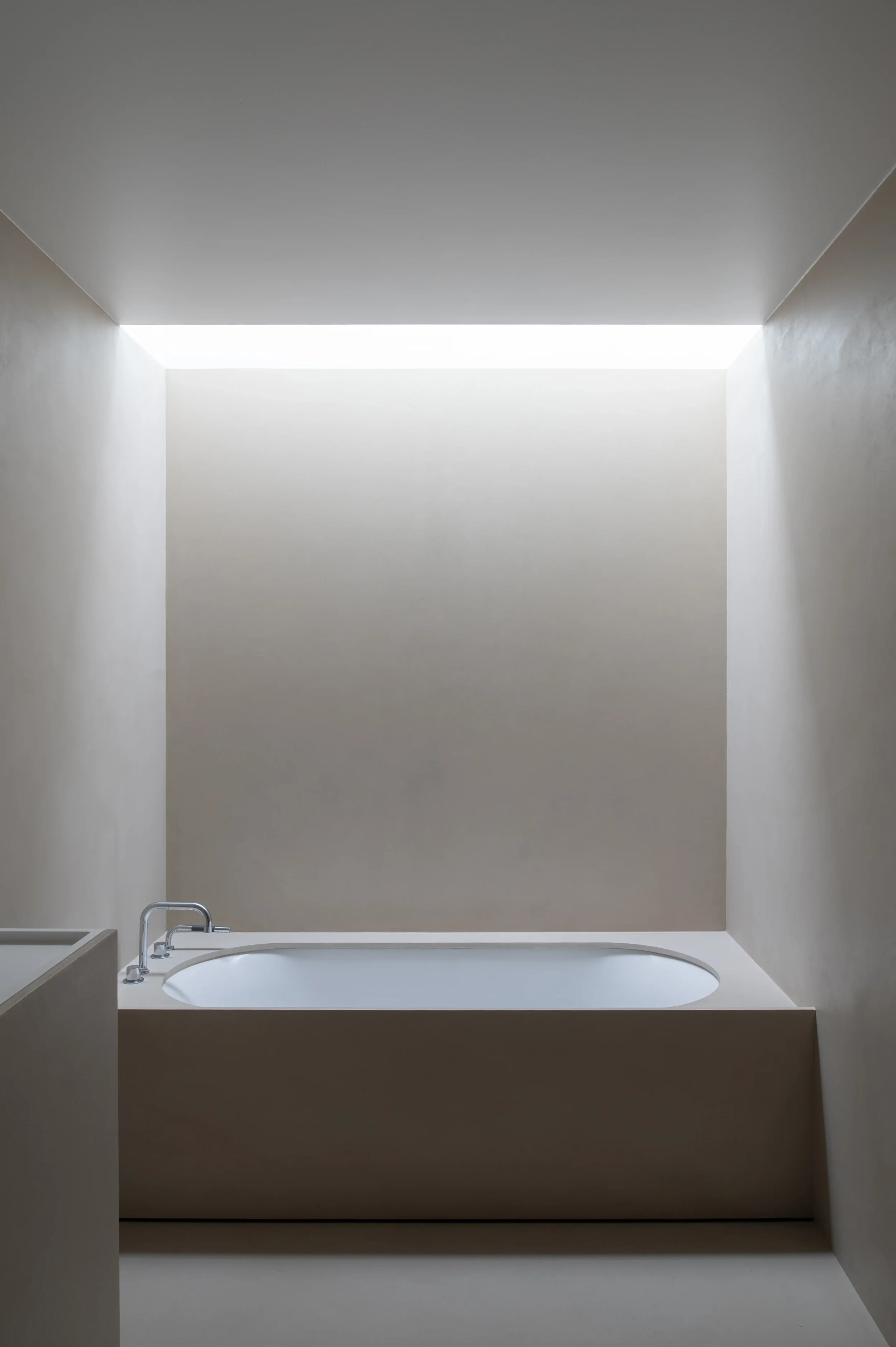 Modern bathroom with a built-in bathtub, faucet, and a neutral color scheme, illuminated by a horizontal skylight.
