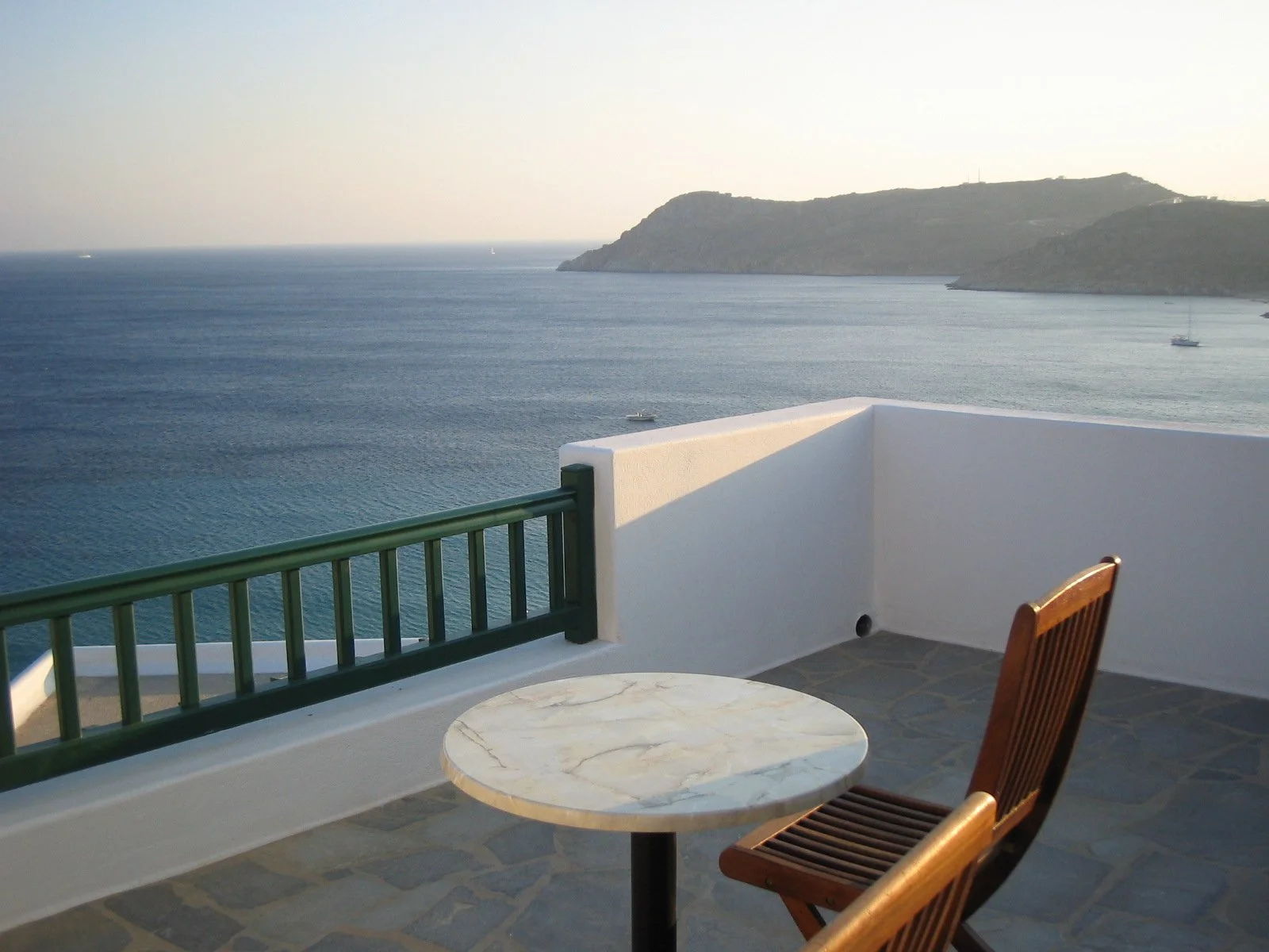 Vista dal balcone con tavolo di marmo, sedia di legno, vista mare e isola con collina