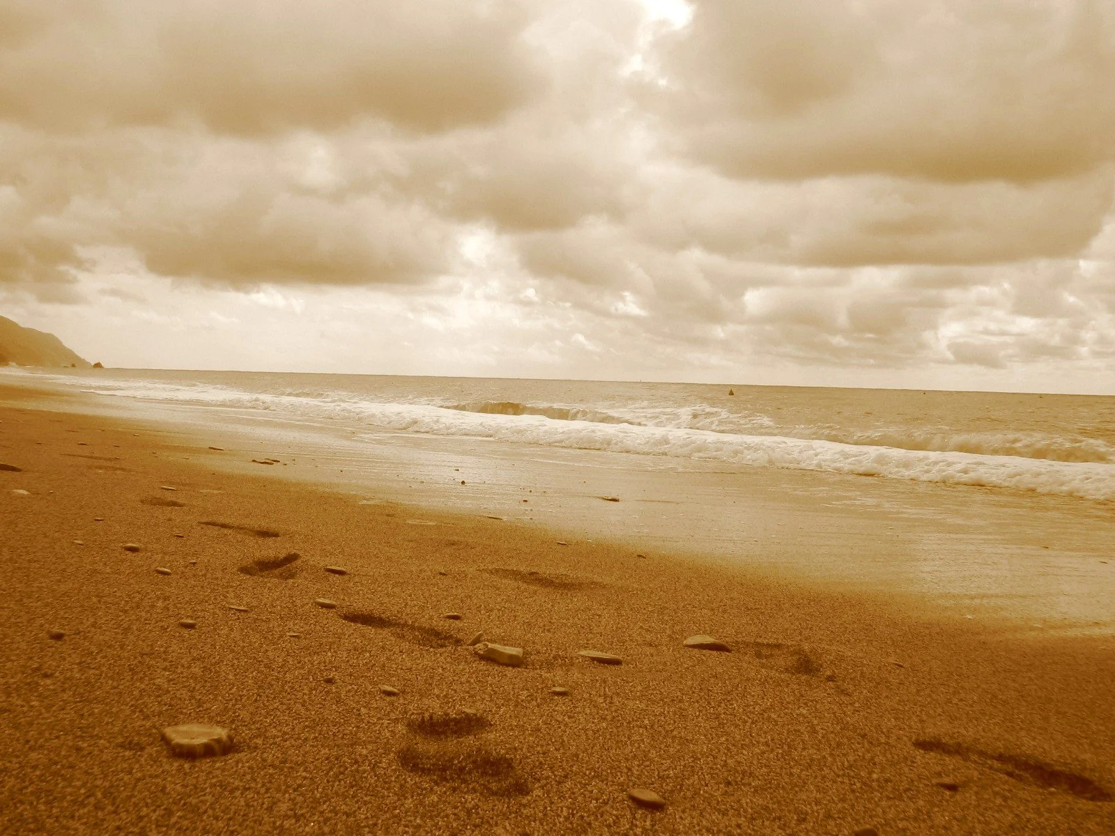 Spiaggia con sabbia, onde del mare e nuvole nel cielo, visibile dall'orizzonte, con alcune pietre sulla battigia.