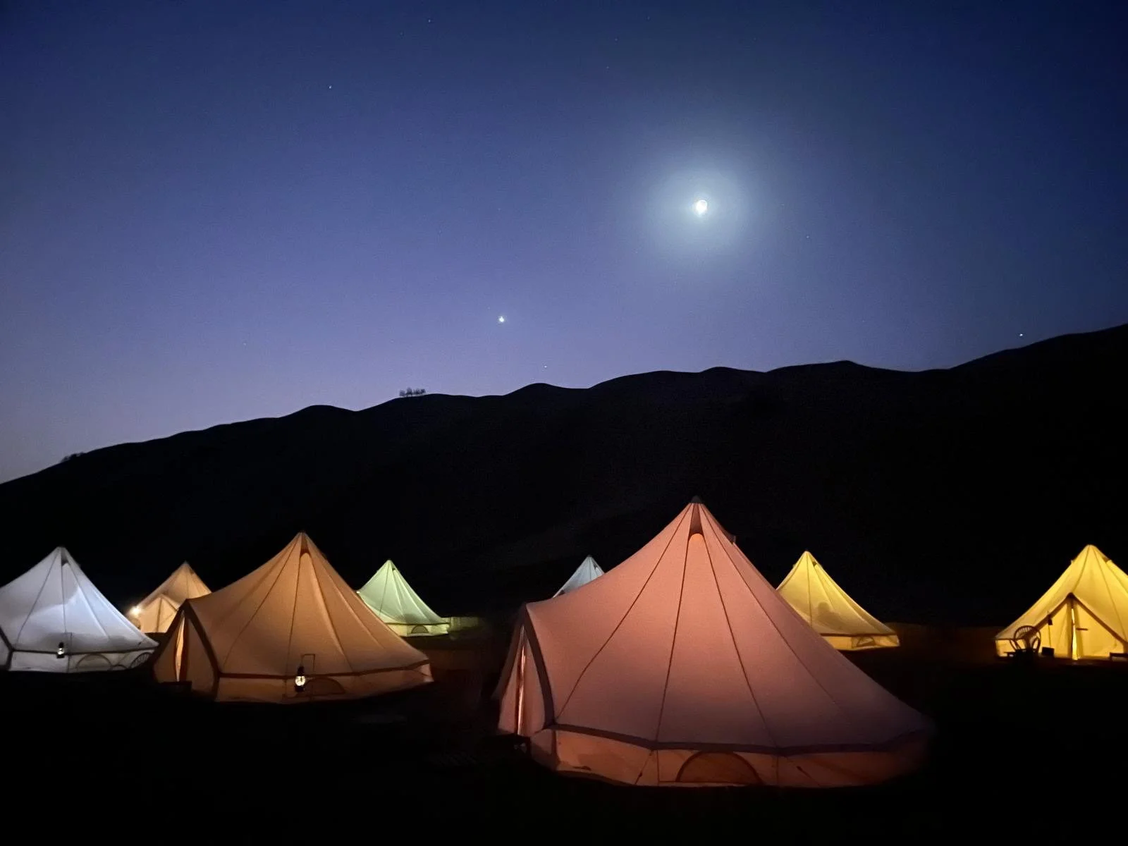 Tende colorate nel deserto sotto il cielo stellato e la luna piena sullo sfondo.