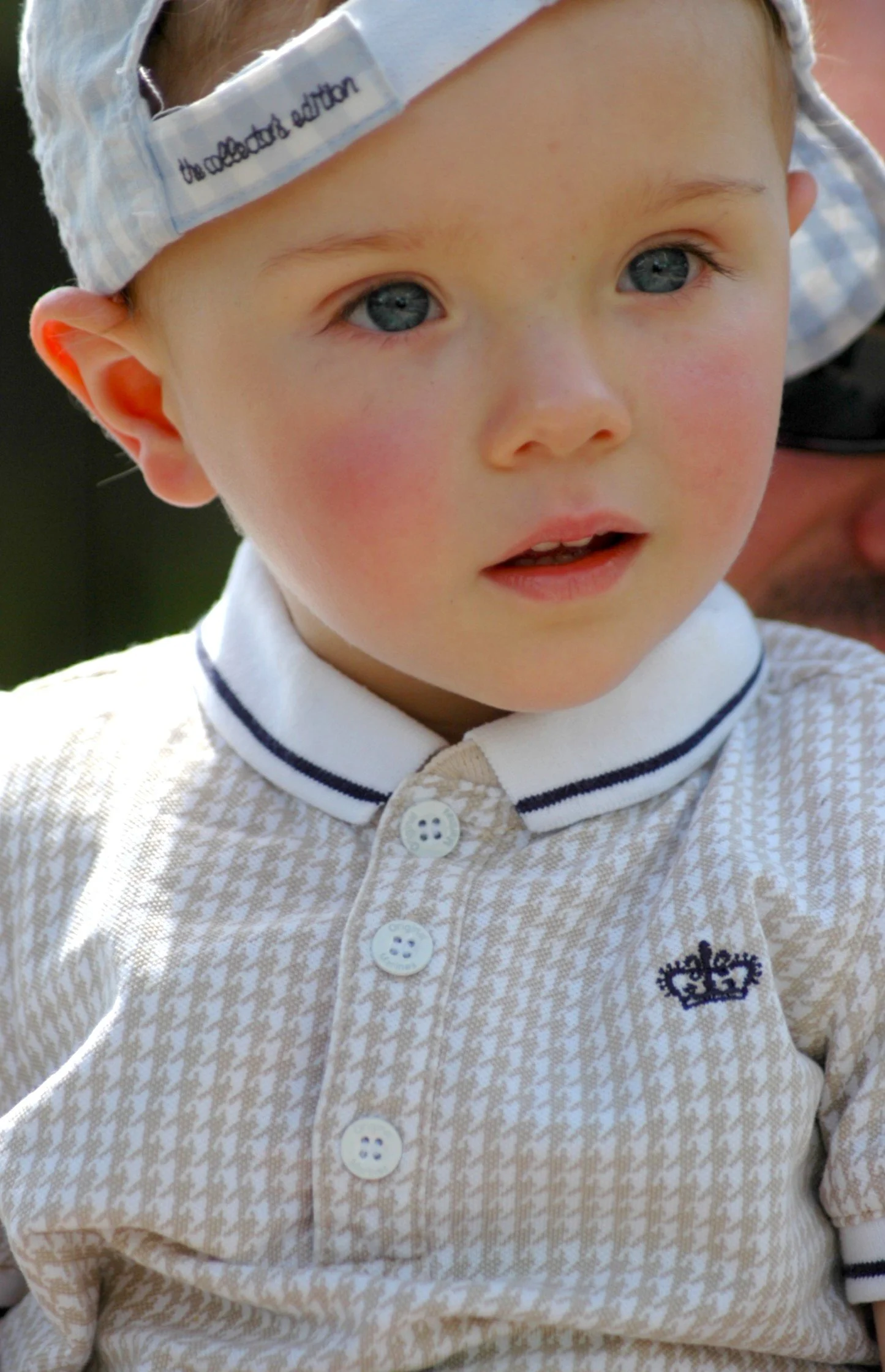  primo piano di un bambino con giacca a maniche lunghe a motivo a houndstooth e colletto con bordo a righe blu e bianca con ricamo di corona sulla sinistra