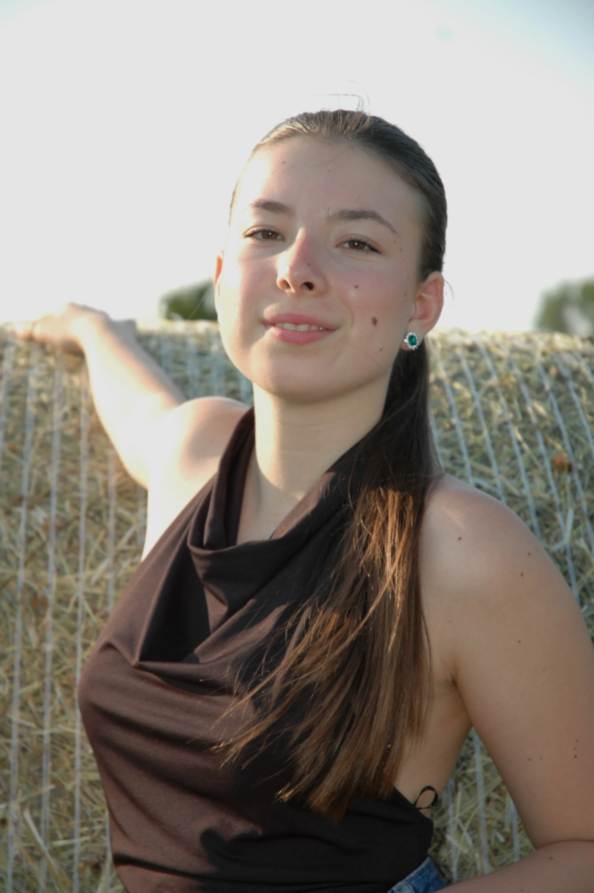 Ragazza con capelli castani e orecchini verdi in un campo, sorridente, che guarda verso la fotocamera.