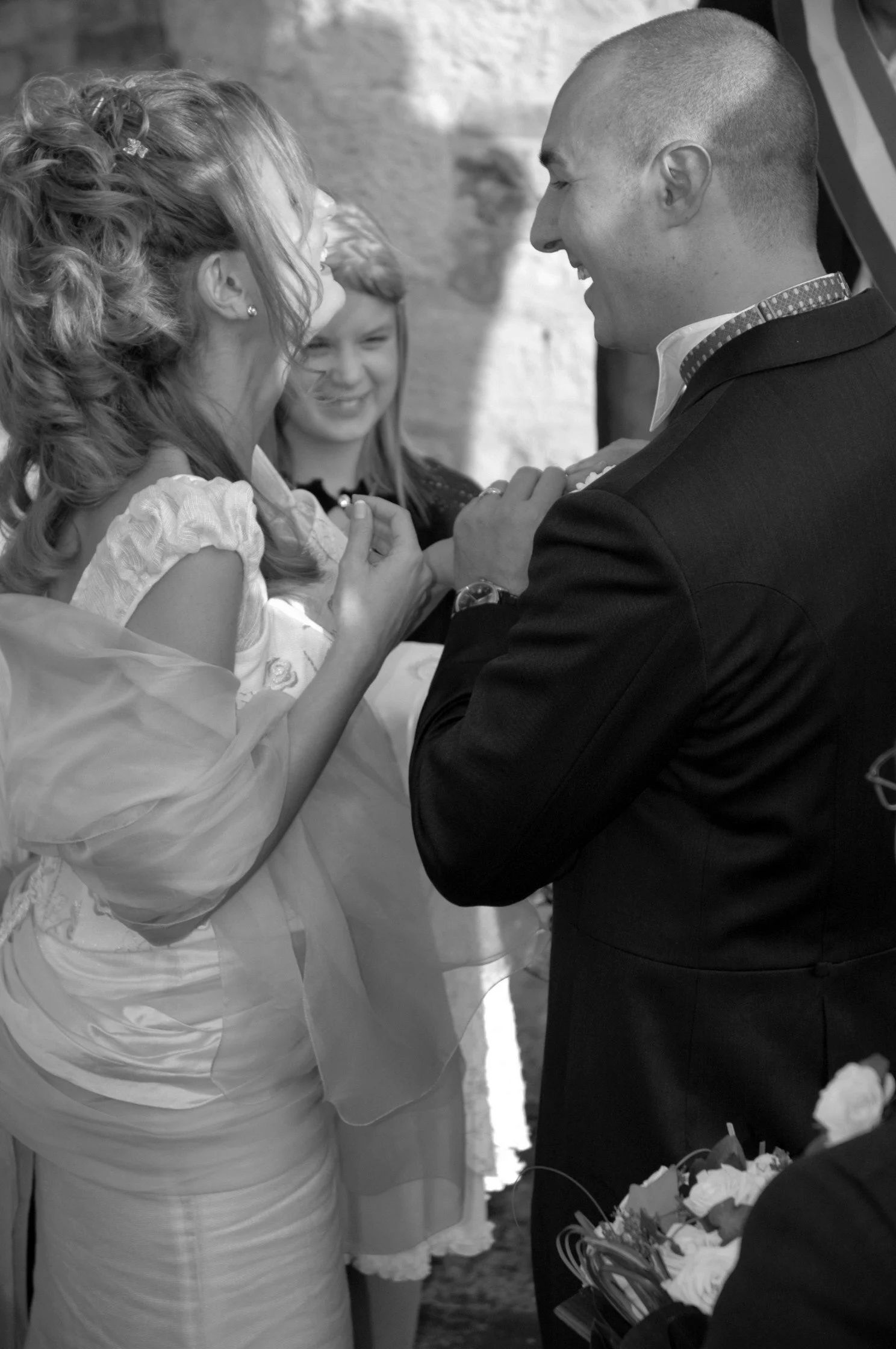 Un uomo e una donna sorridenti si tengono per mano, con una donna più giovane in secondo piano, in un momento di felicità o celebrazione.