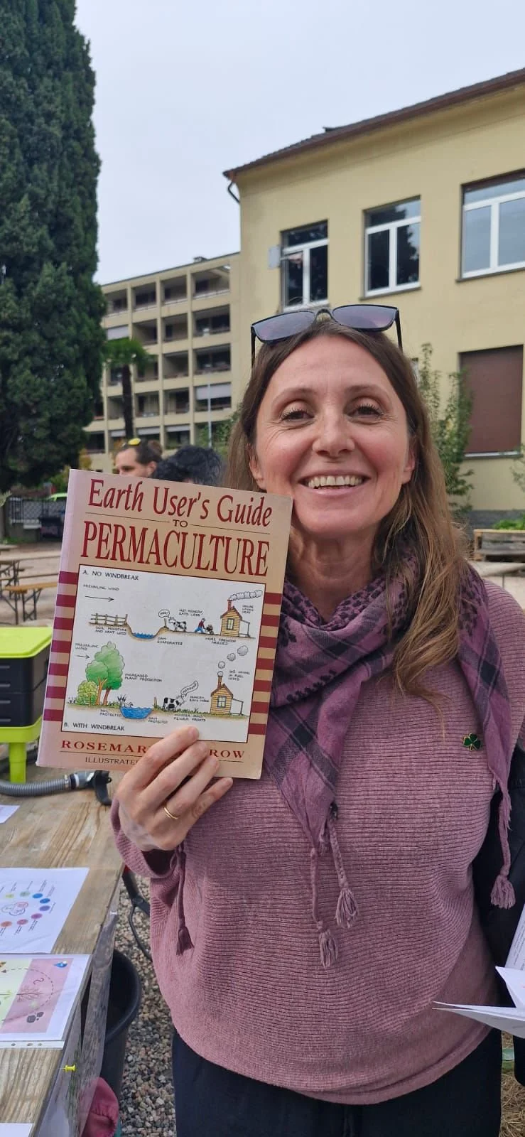 A smiling woman outdoors holding a book titled "Earth User's Guide to Permaculture".