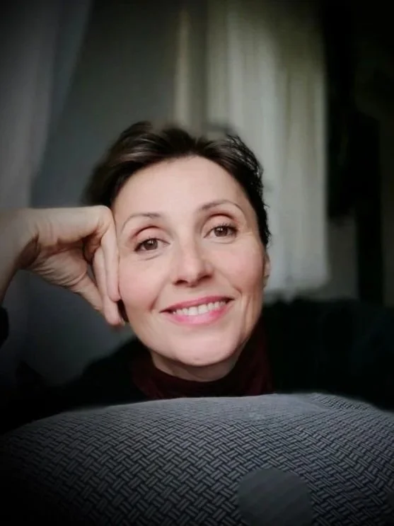 A woman with short dark hair smiling and resting her head on her hand.