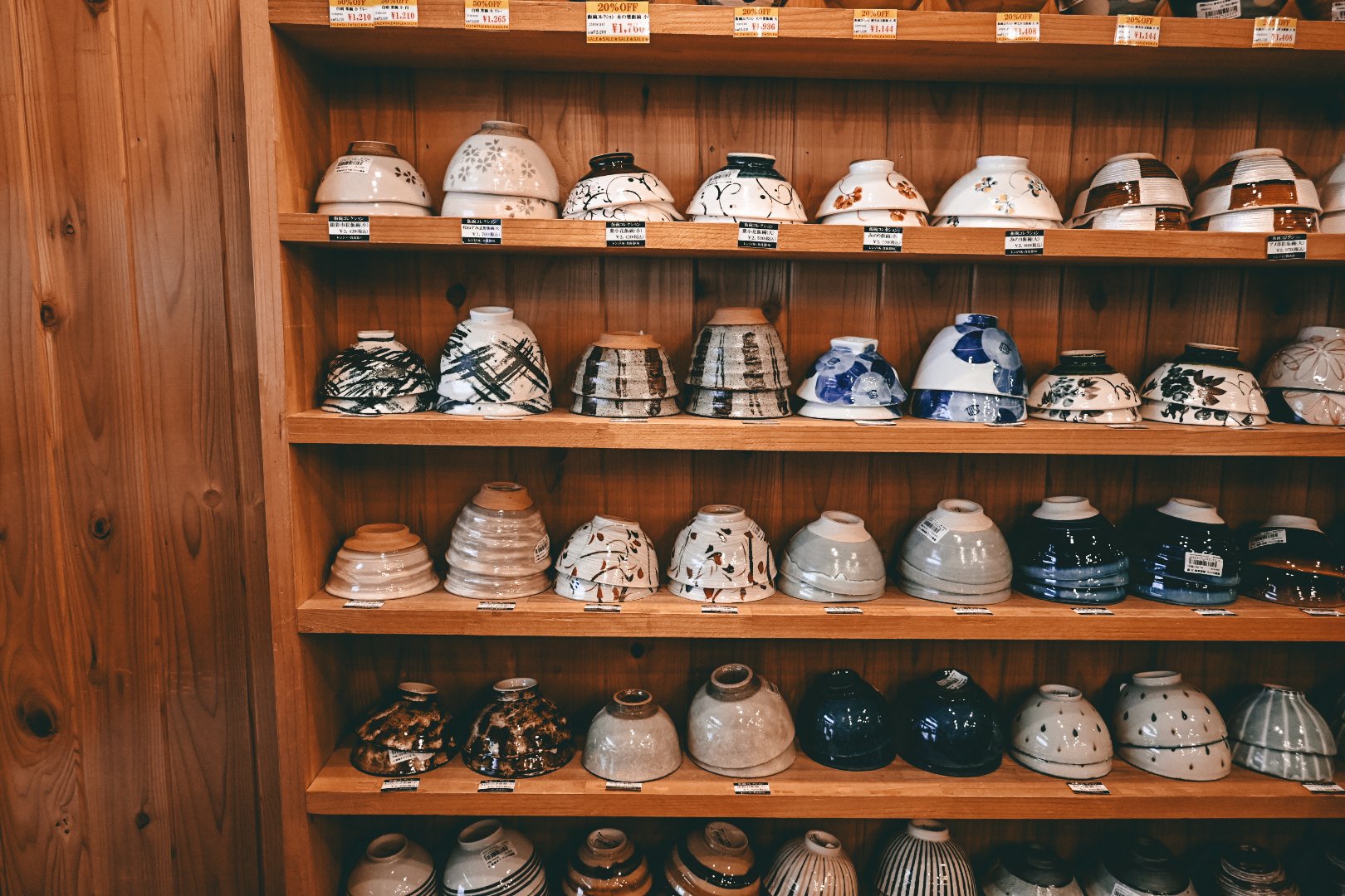 Wooden display shelf filled with various decorative ceramic bowls arranged in rows, featuring different patterns and colors.