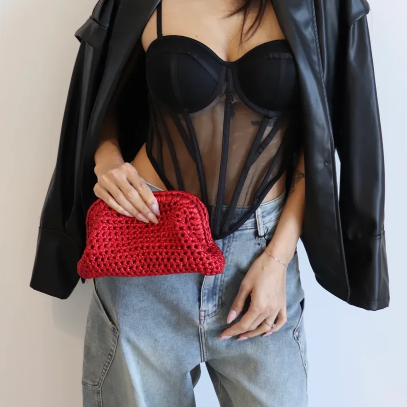 Donna con giacca di pelle indossa un top trasparente e una borsa rossa in mano.