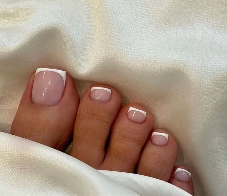 Ongles de pieds avec une manucure française sur un lit en satin blanc.