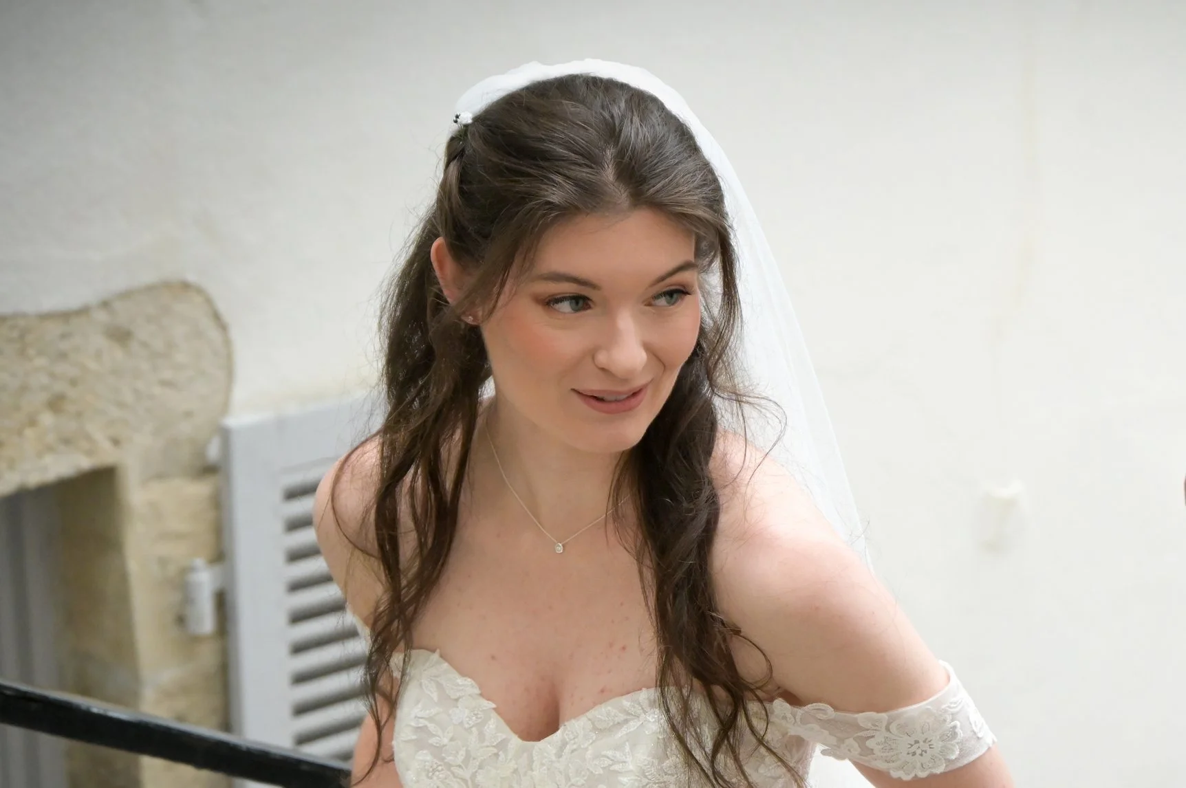 Jeune femme en robe de mariée avec un voile, souriant et regardant de côté, dans un environnement intérieur simple.