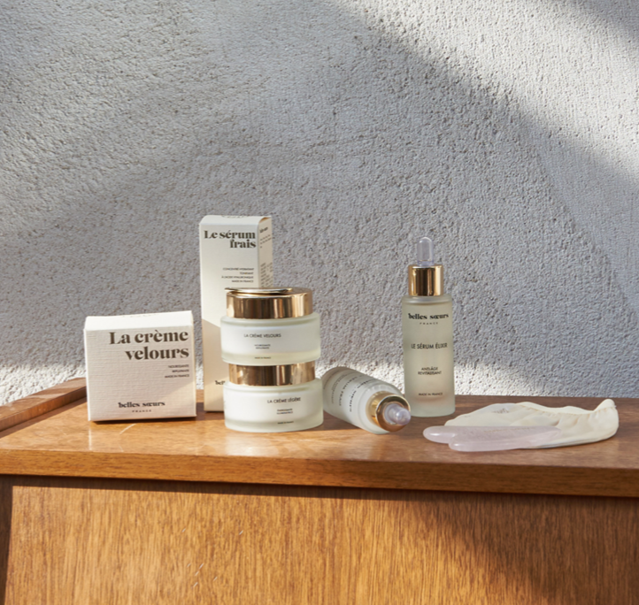 Produits de soins de la peau sur une table en bois, comprenant des crèmes, un sérum et une pipette, dans un éclairage naturel.