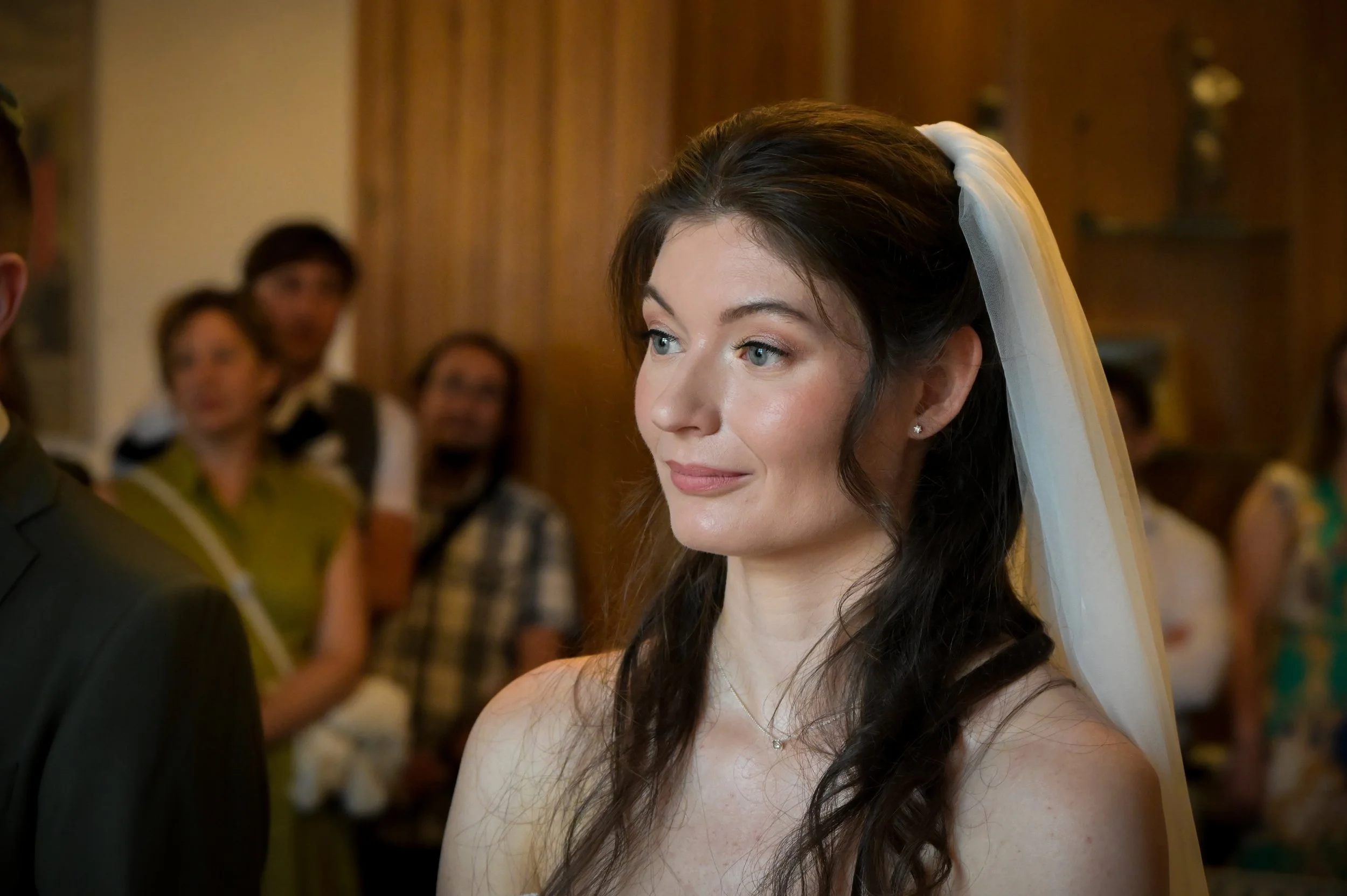 Femme lors de son mariage portant une robe blanche et un voile dans une salle avec des invités en arrière-plan.