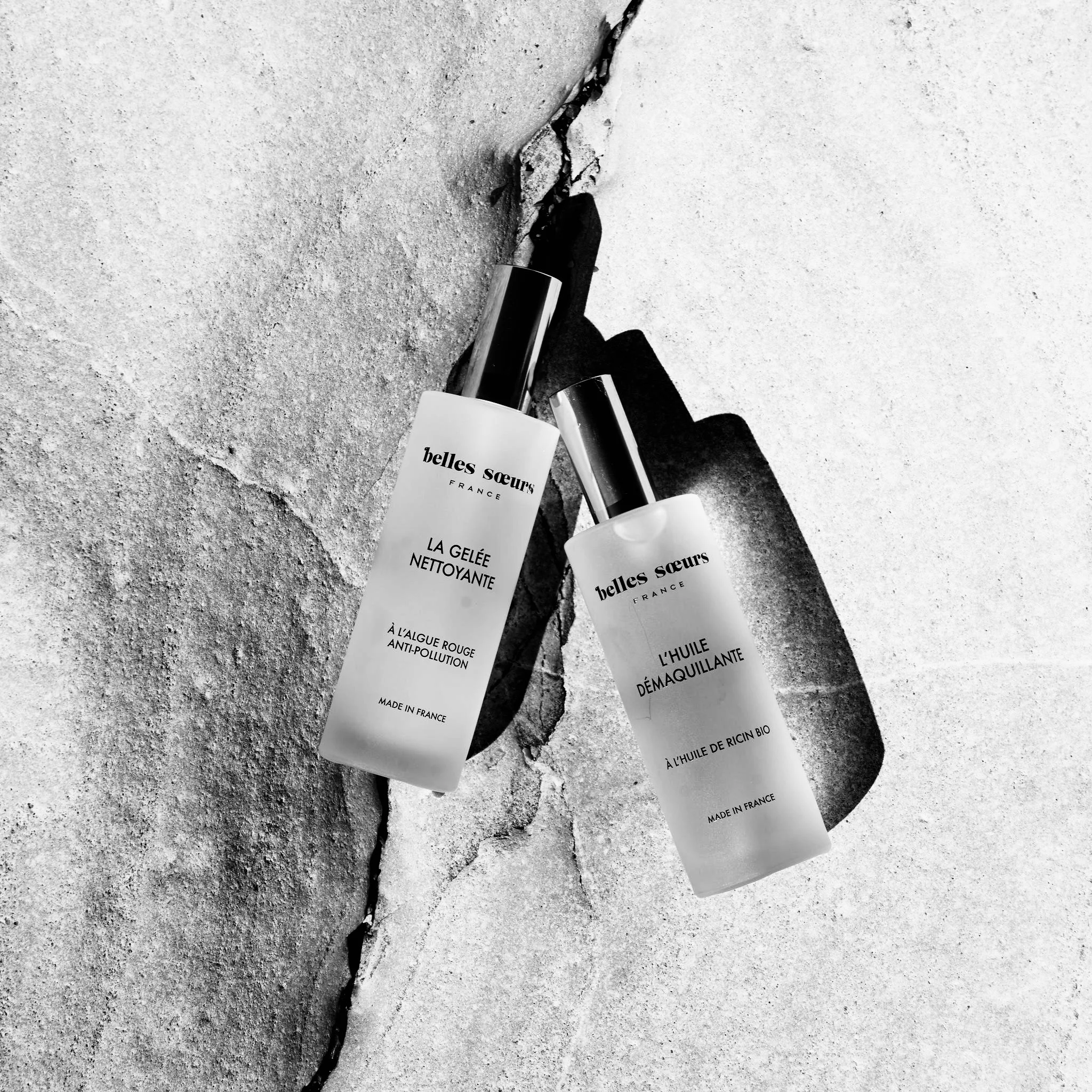 Bouteilles de produits de beauté ou de soins sur un sol en béton, en noir et blanc.