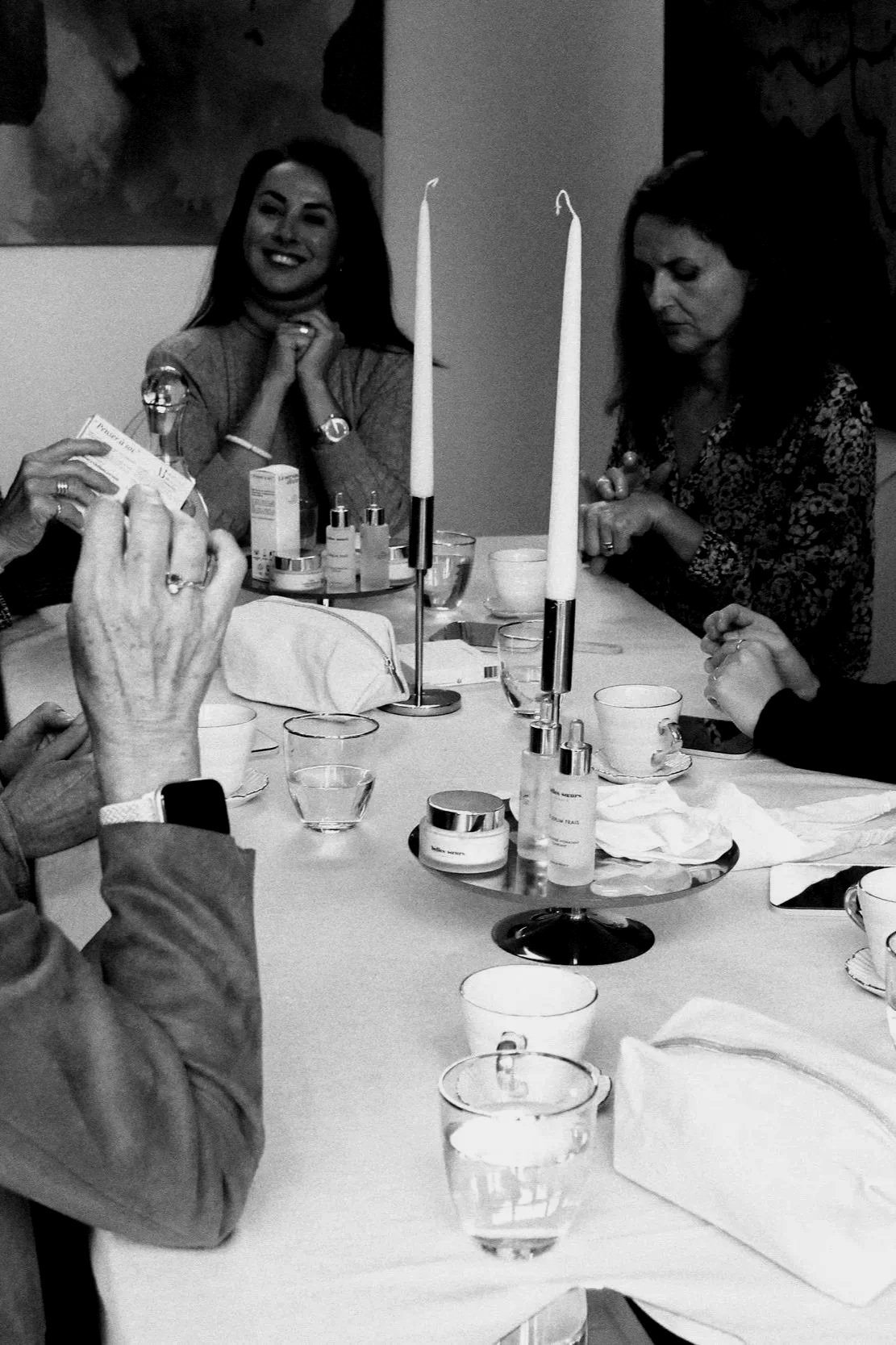Groupe de personnes assises autour d'une table lors d'une réunion ou d'une célébration, avec des bougies et des verres d'eau.