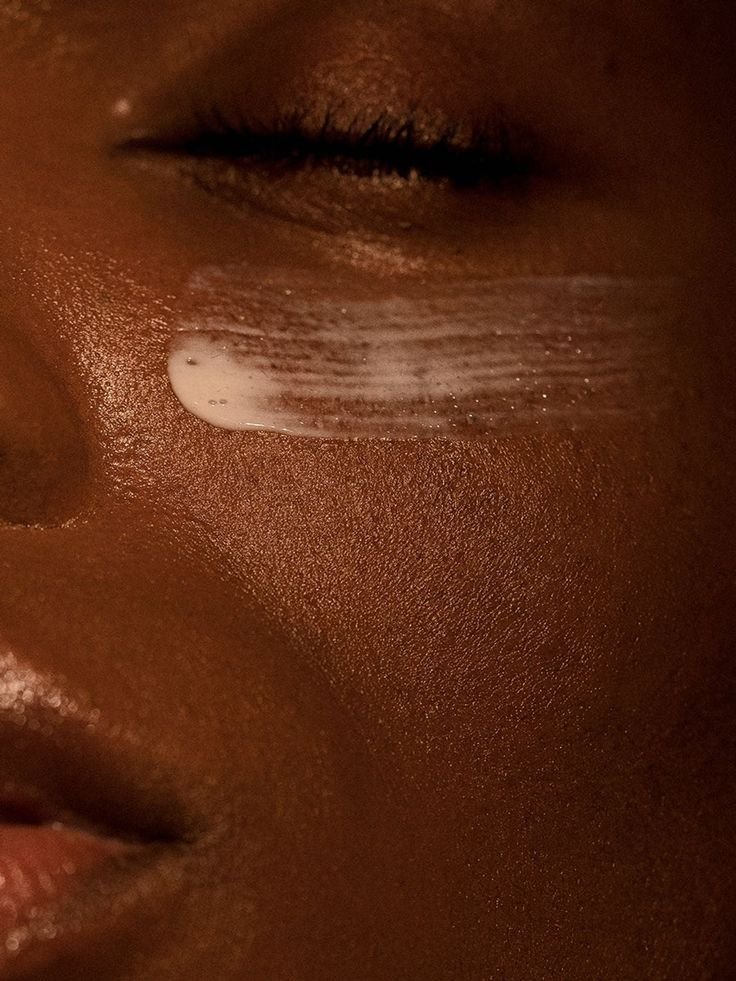 Zoom sur le visage d'une personne noire avec un peu de crème ou de gel blanc sur la joue, peau bronzée et lèvres visibles.