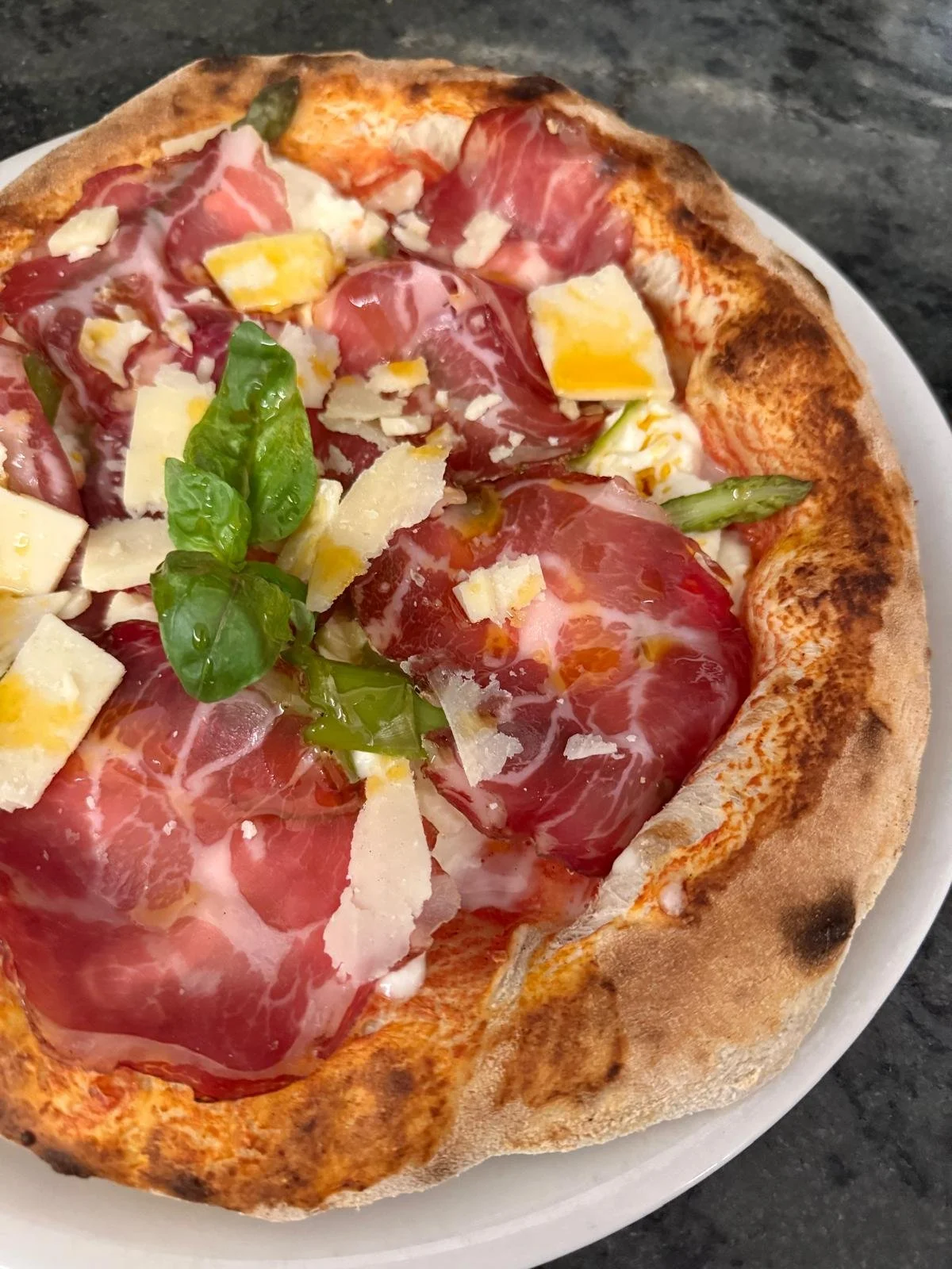 Pizza con prosciutto, rucola, scaglie di parmigiano, e mozzarella.