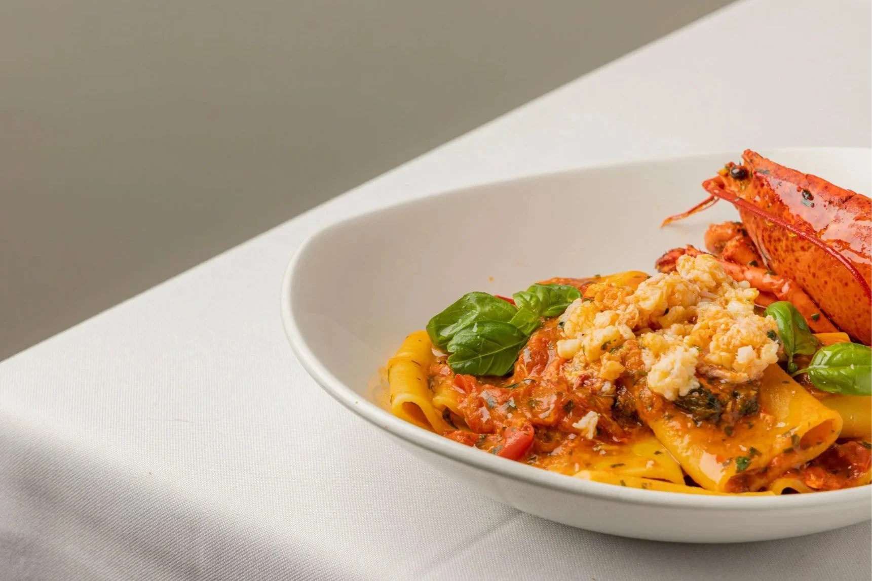 Piatto di pasta con sugo di pomodoro, basilico, ricotta salata, accompagnato da crostaceo d'aragosta.