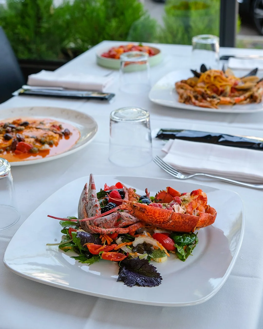 Piatti di pasta e un piatto di insalata con aragosta in un ristorante all'aperto.