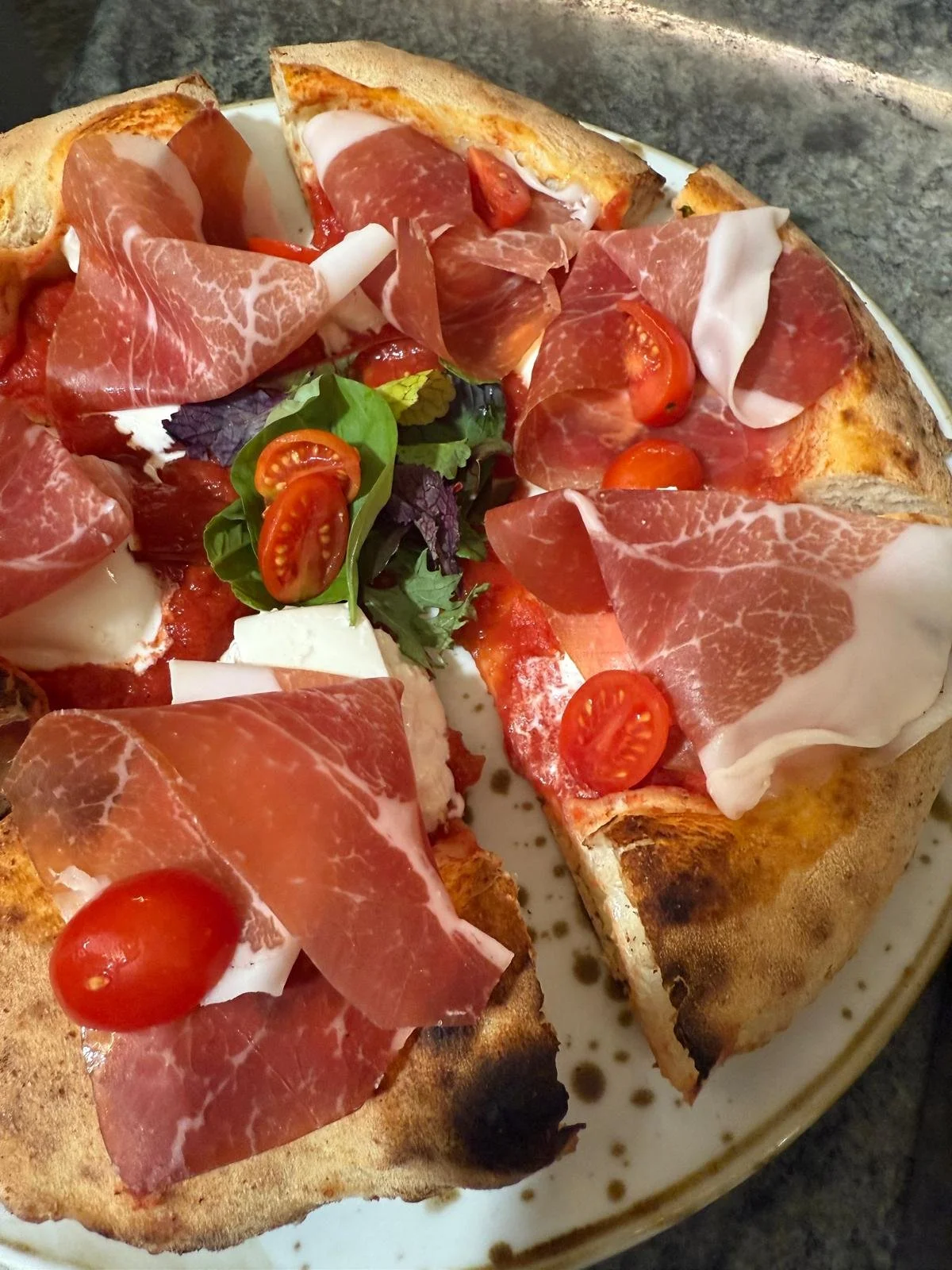 Pizza con prosciutto crudo, pomodorini e insalata mista.