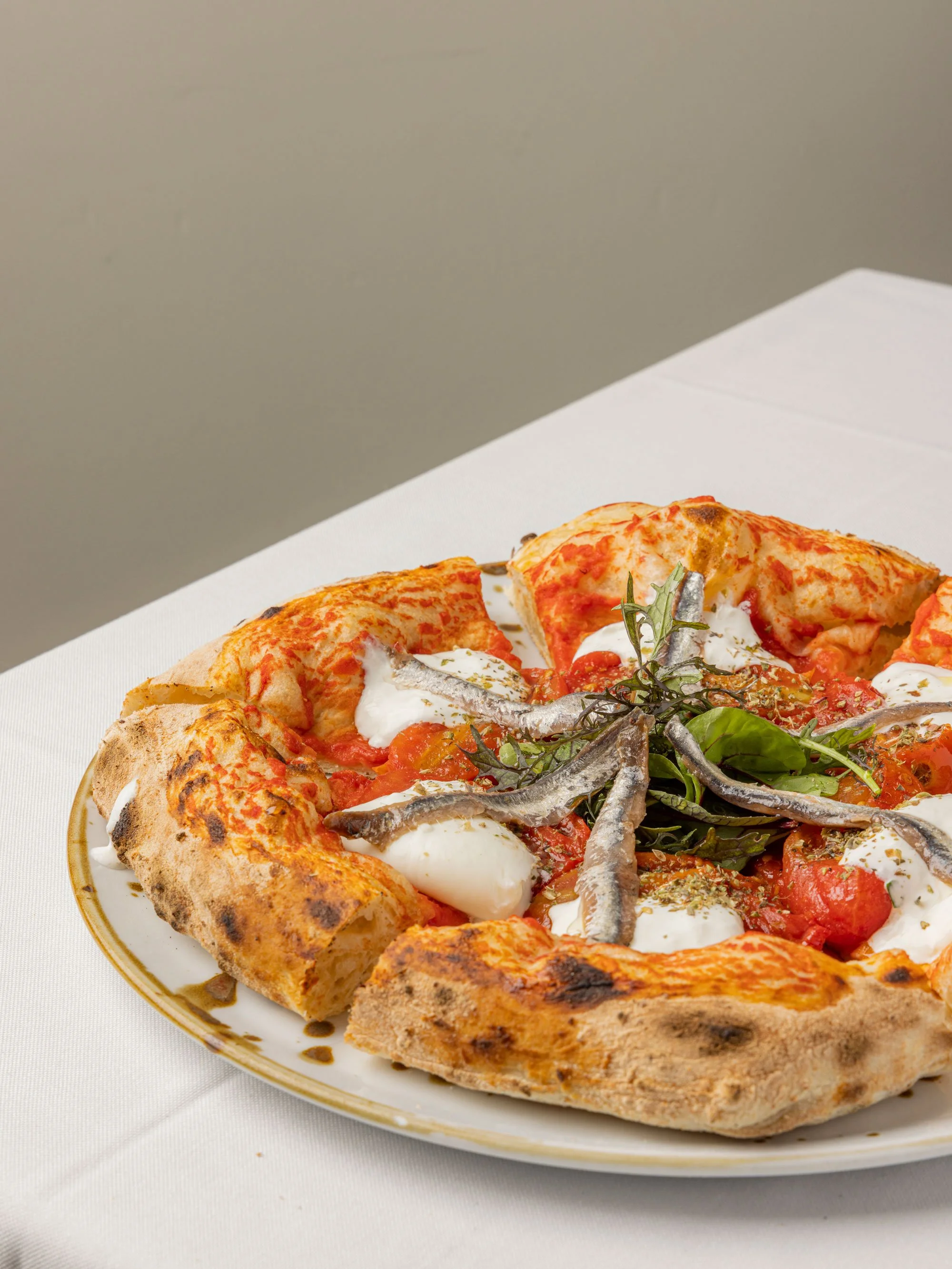 Pizza con pomodoro, mozzarella, acciughe, erbe aromatiche e basilico su un piatto bianco.