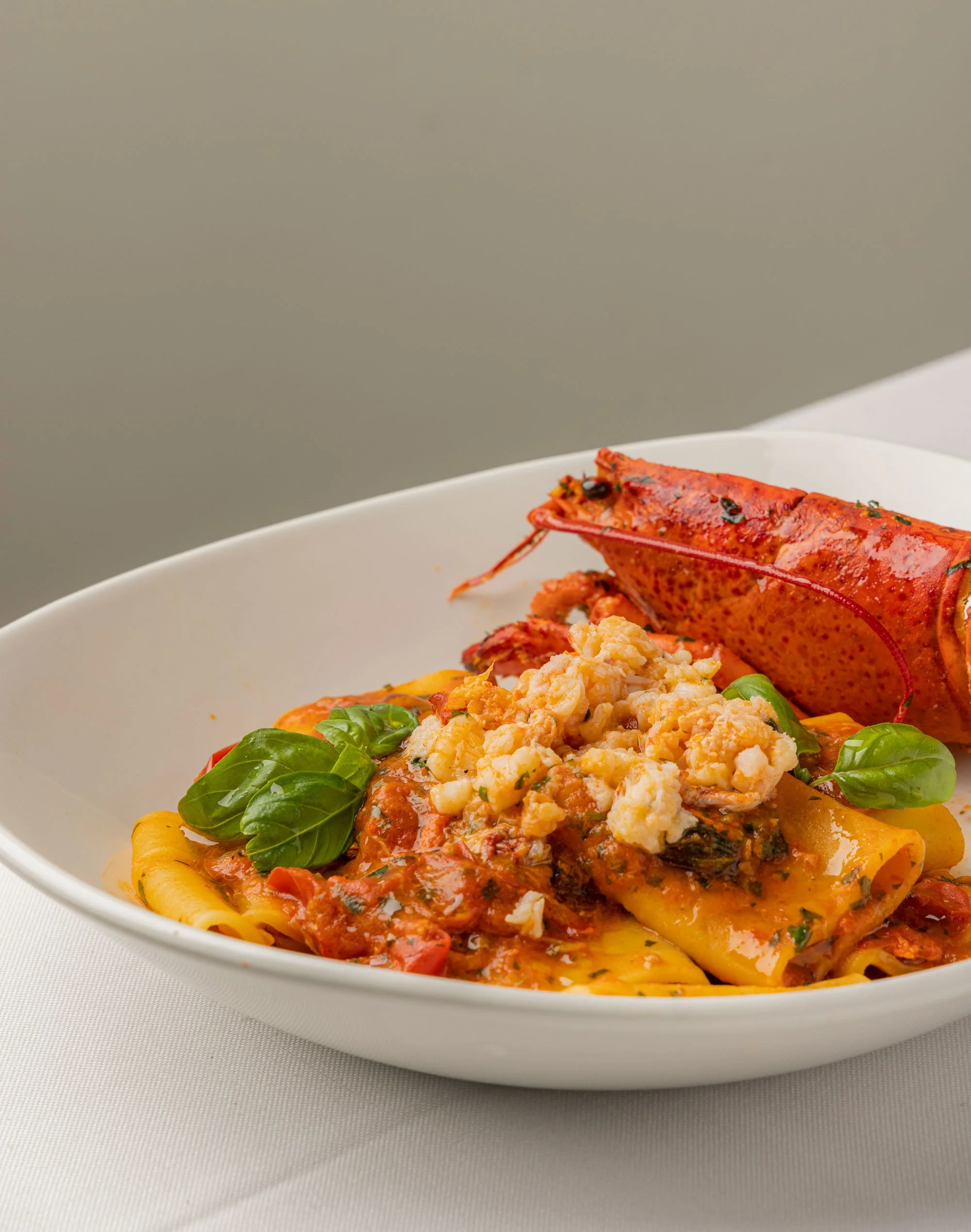 Piatto di pasta con sugo di pomodoro, con erbe e formaggio, decorato con foglie di basilico e un'astice.