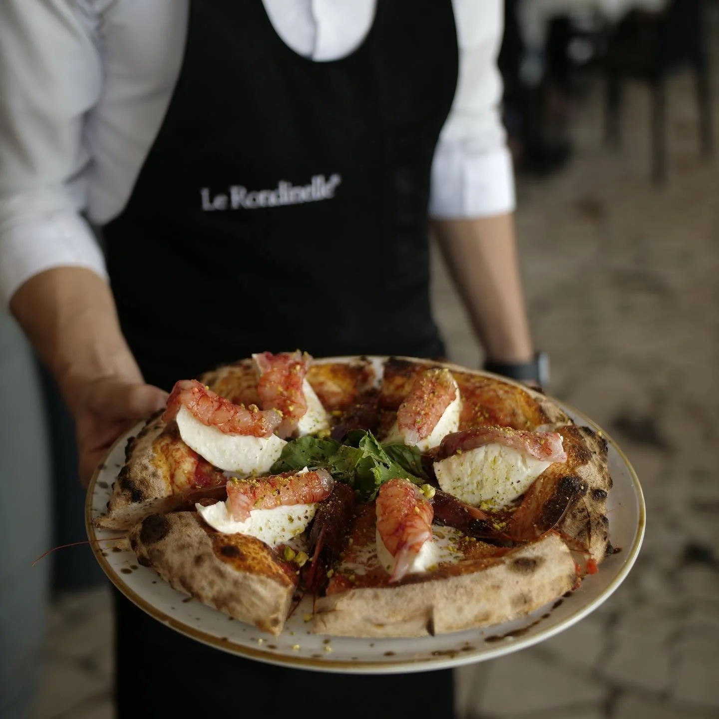 Persona che tiene una pizza con mozzarella, gamberi e basilico.