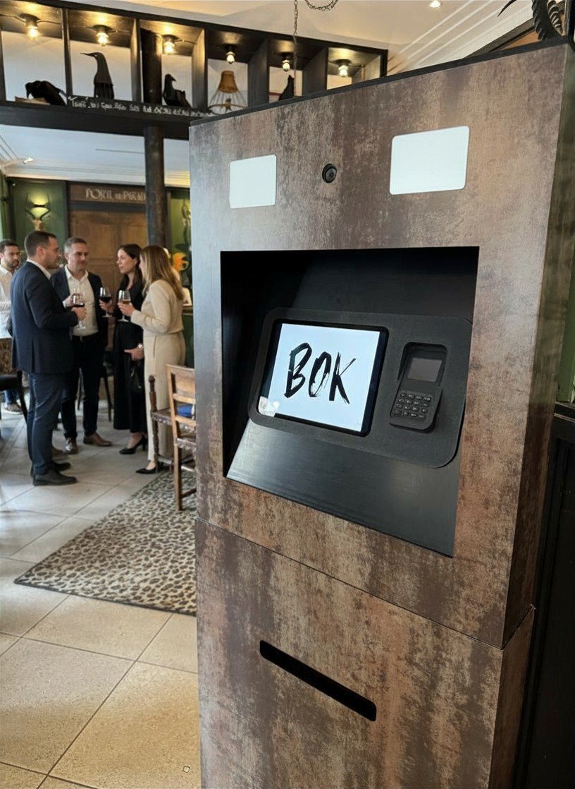 Un kiosque à billets dans un restaurant ou bar, avec un écran affichant le mot 'BOX' en écritures manuscrites.
