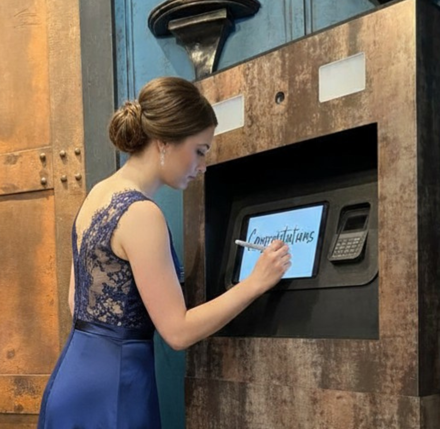 Une femme habillée en robe bleue écrivant le mot "Congratulations" sur un écran tactile