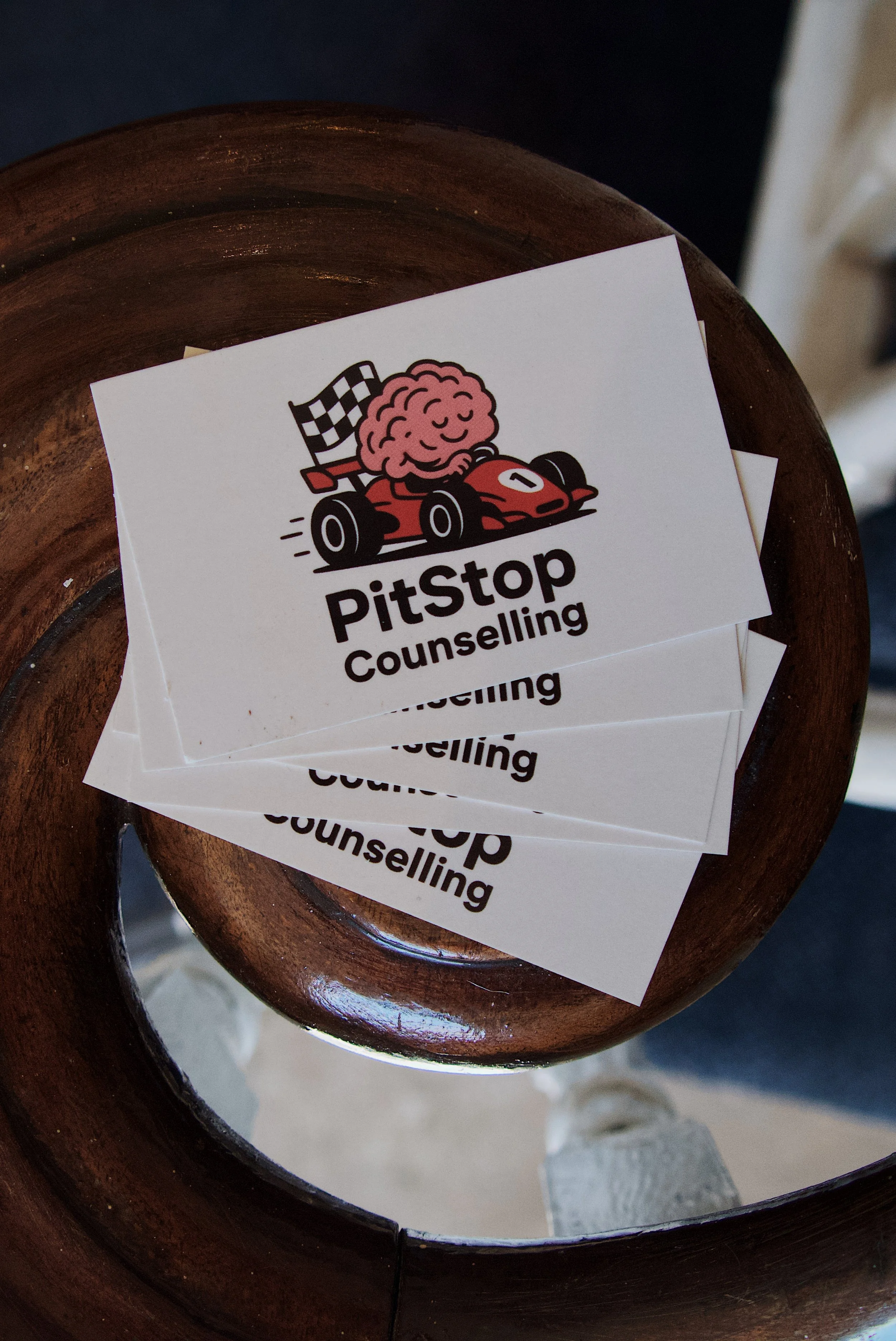 Business card for PitStop Counselling resting on a curved wooden surface, photographed from above.