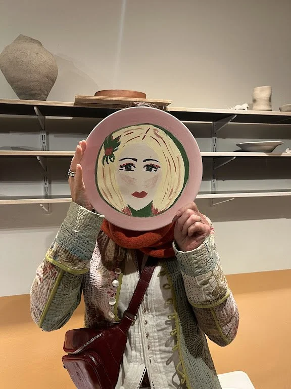 Persoon houdt een bord voor haar gezicht met een getekend portret van een vrouw met blonde haren en rode lippen.