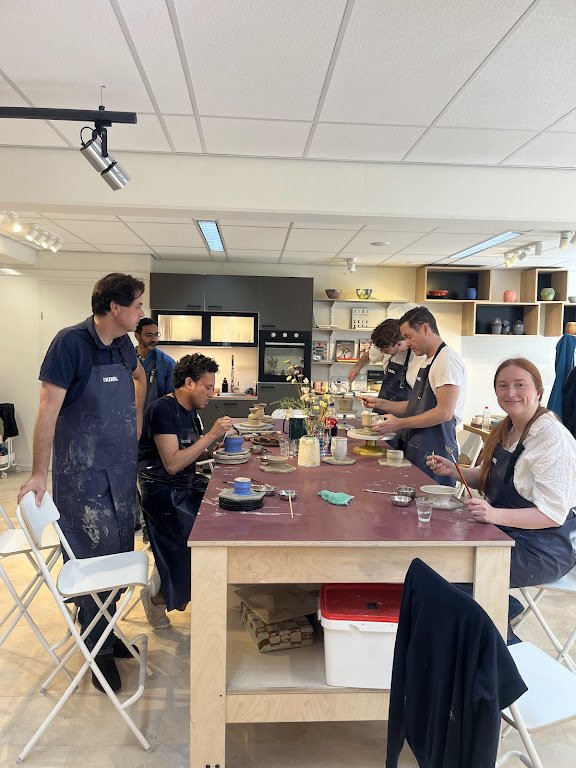 Vrouw die potten en keramische voorwerpen beschildert, en anderen die in een atelier keramiek maken.