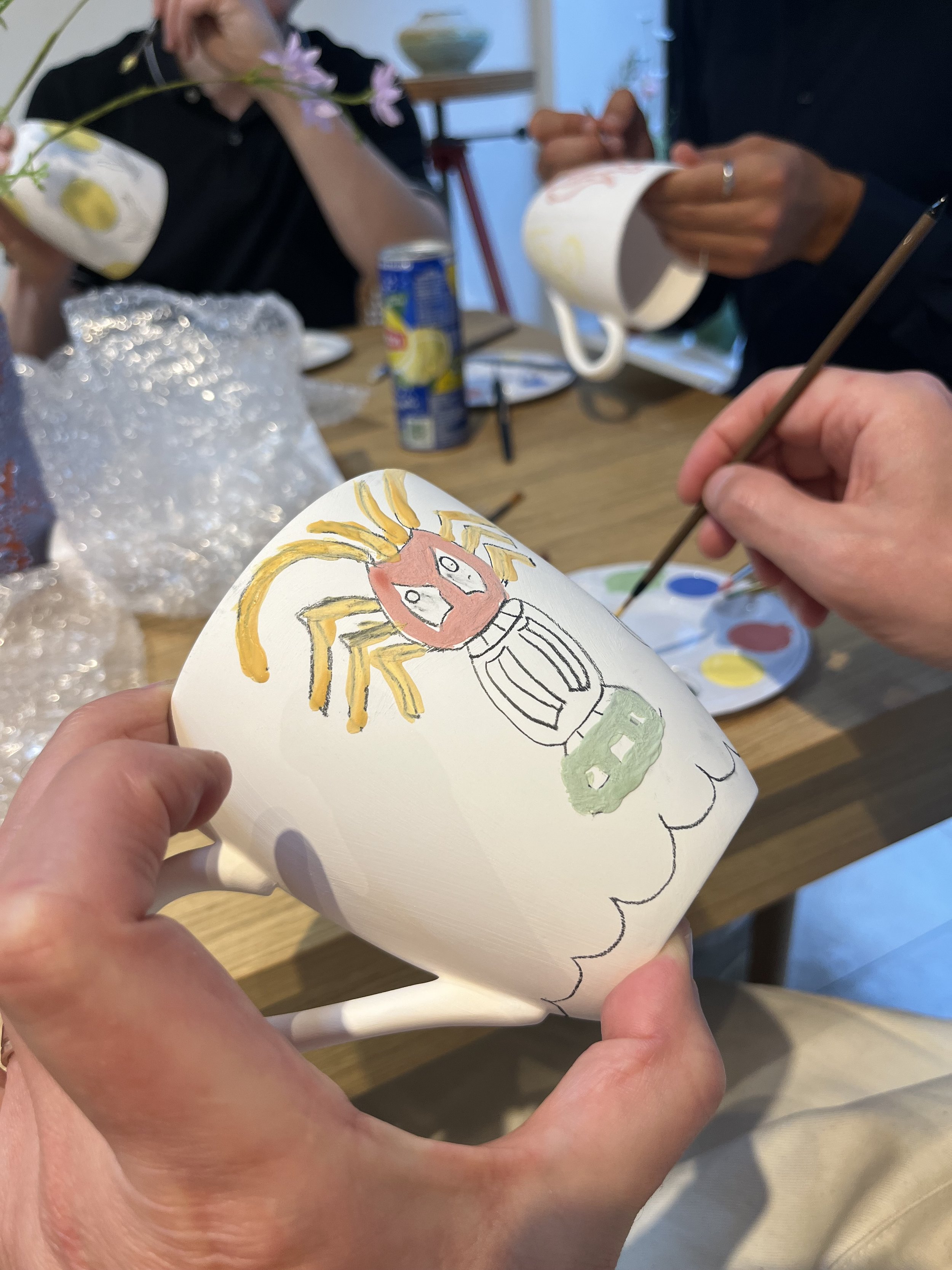Persoon die een tekening van een kreeft met een gezicht en een auto op een biscuit mok maakt.