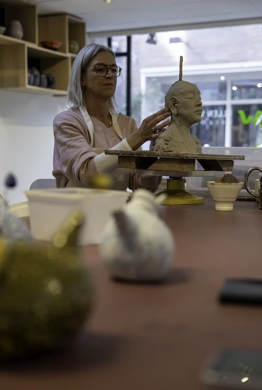 Kunstenares werkt aan een papier-maché beeld in een atelier met grote ramen.