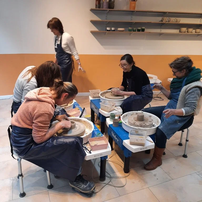Vijf mensen die keramiek potten maken met draaischijven in een kunstwerkplaats.