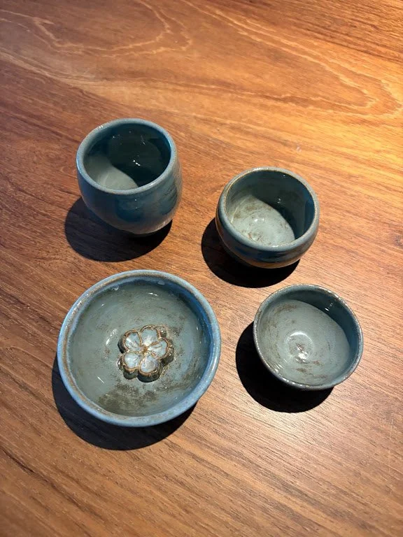 Vier kleine groene keramische schaaltjes en kopjes op een houten tafel, één schaaltje met een bloemvormige afwerking onderaan.