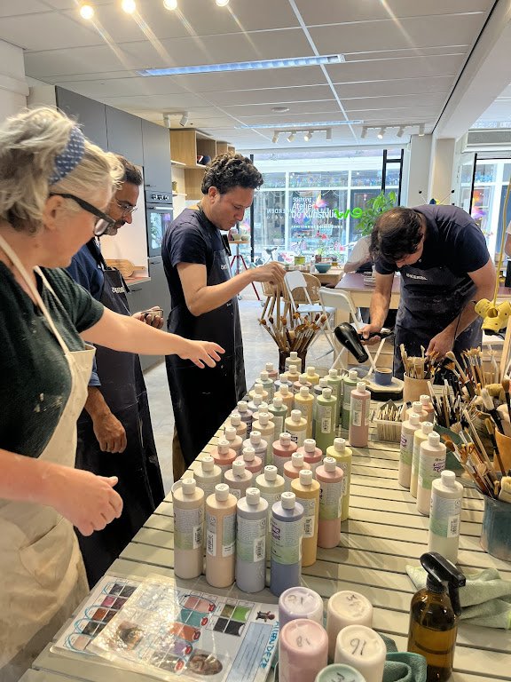 Mensen die deelnemen aan een workshop met verf- en kunstenaarsbenodigdheden in een moderne, lichte ruimte.