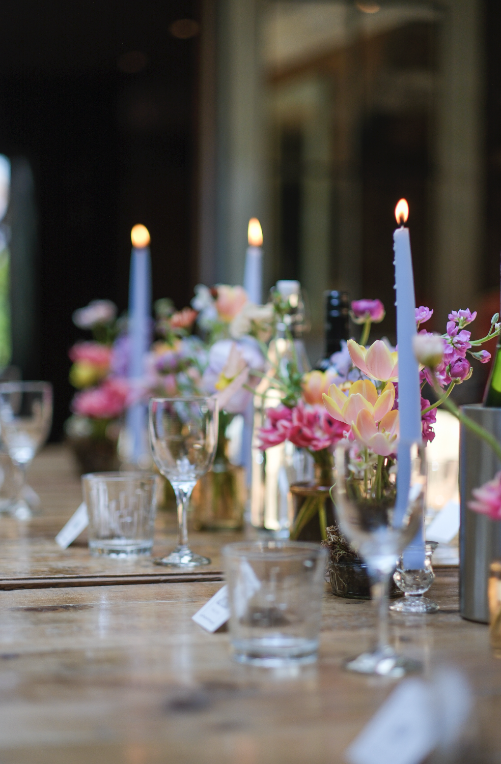 Table decorated with pink and white flowers, tall white candles, and glassware, set for a celebration or dinner event.