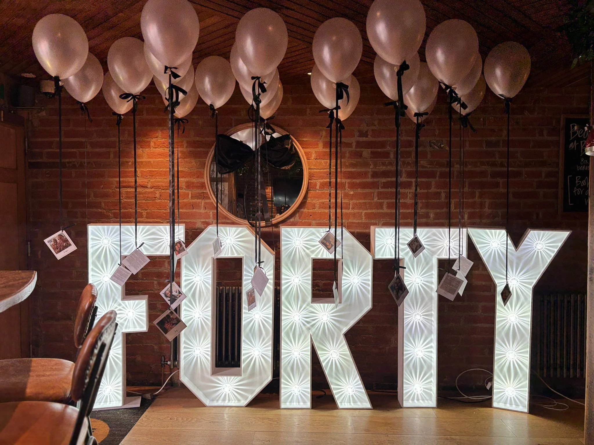 Decorative display of illuminated white letters spelling 'LOVE' with photographs hanging on black strings in front of a brick wall in a cozy indoor setting.