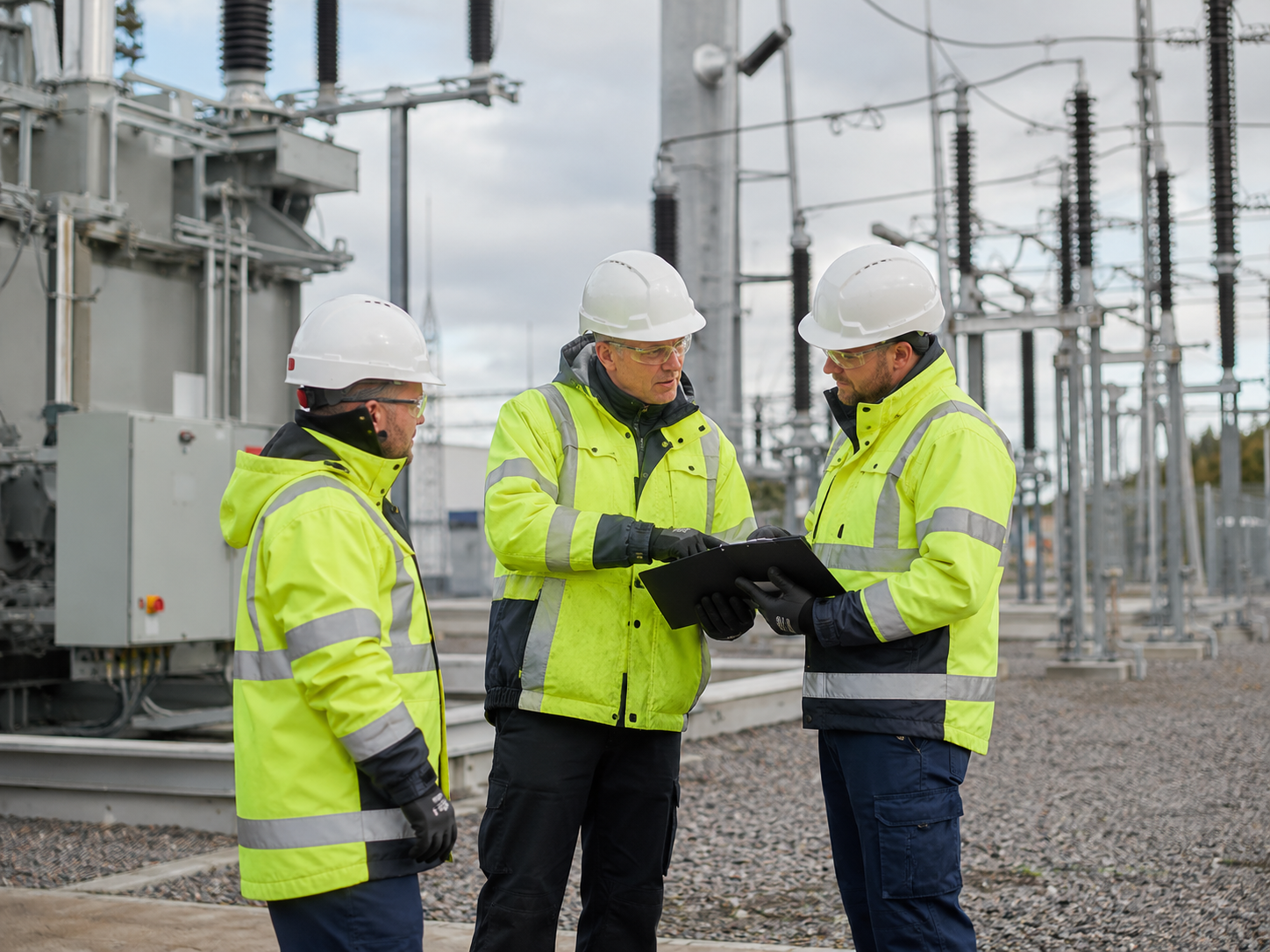 Electrical network workers in high-visibility PPE reviewing project information at a grid infrastructure site.