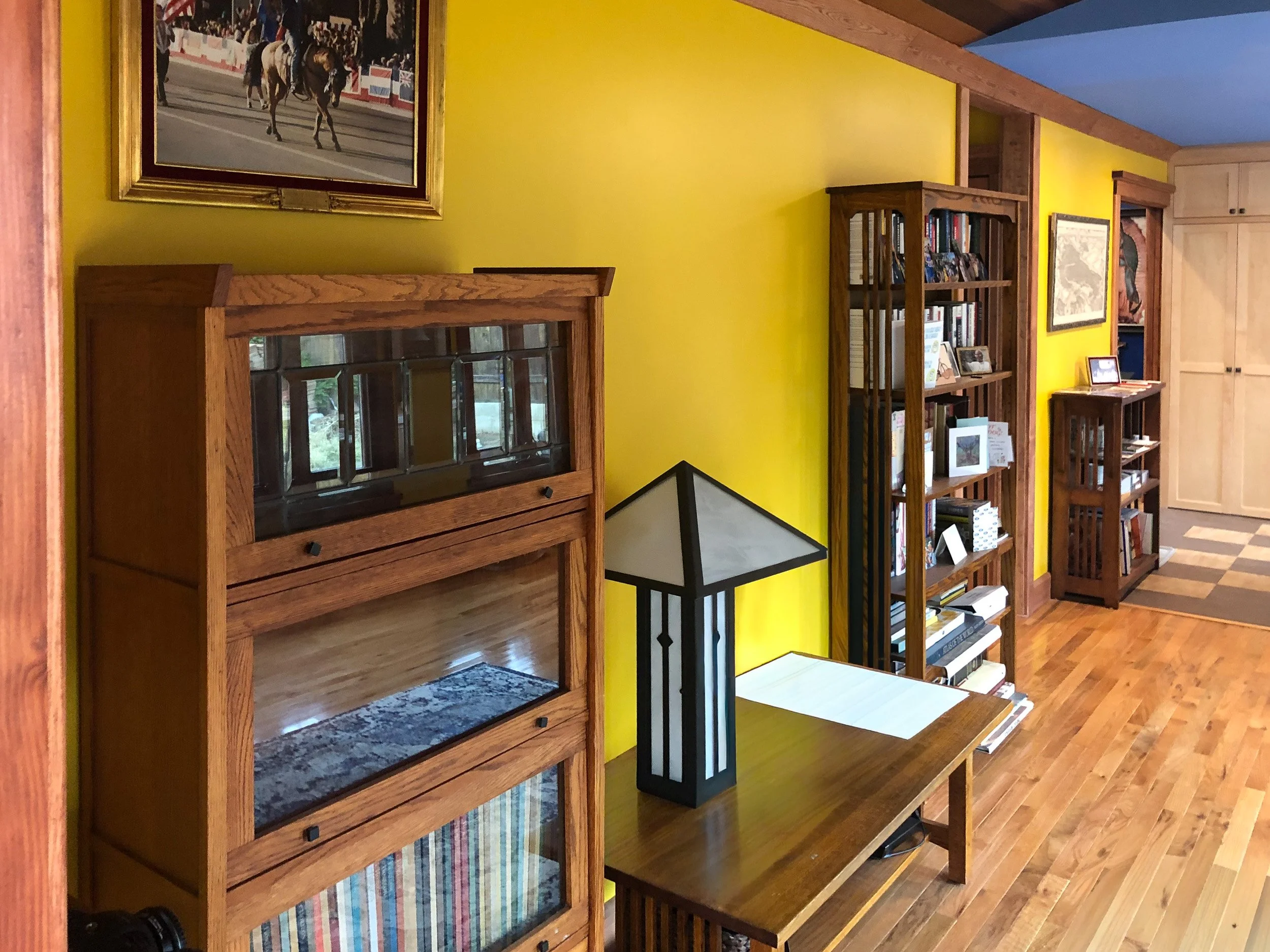 Selling of books and framed paintings in a living room with yellow walls and wooden furniture.
