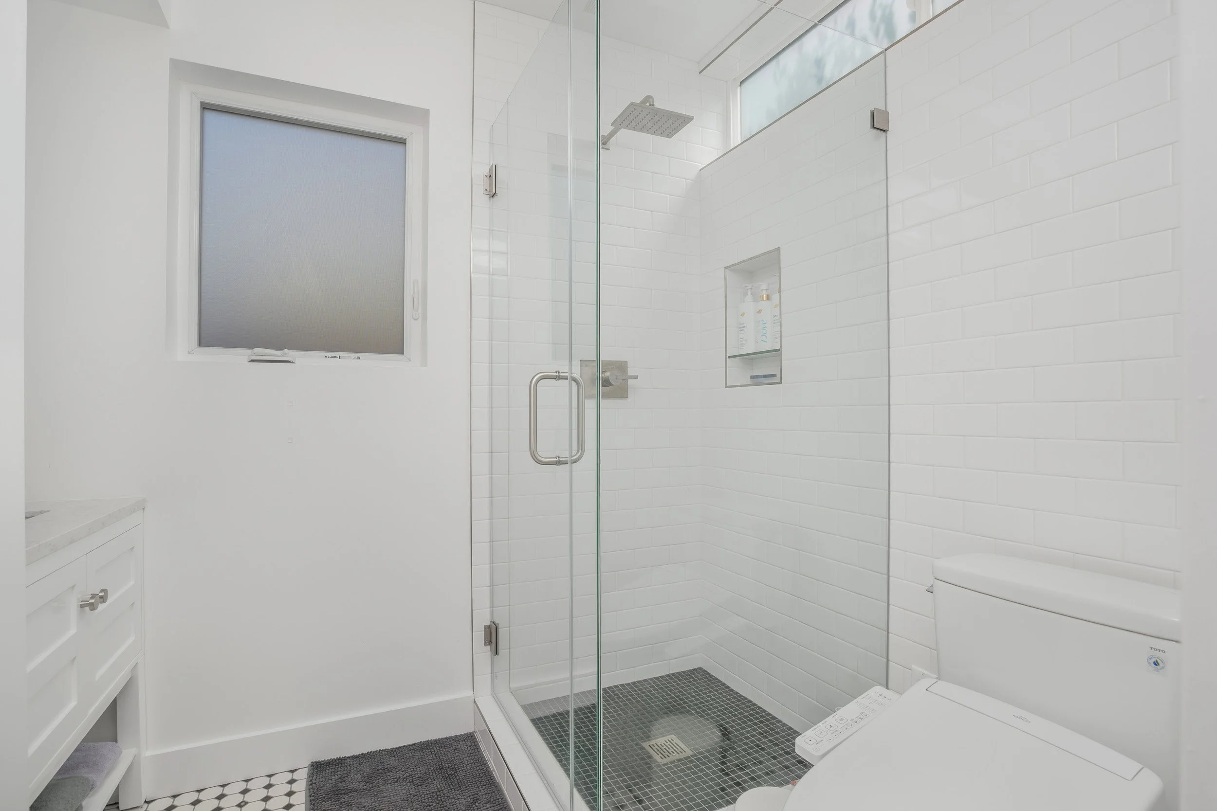 Modern bathroom with a glass shower enclosure, white subway tile walls, a small window, and a toilet.